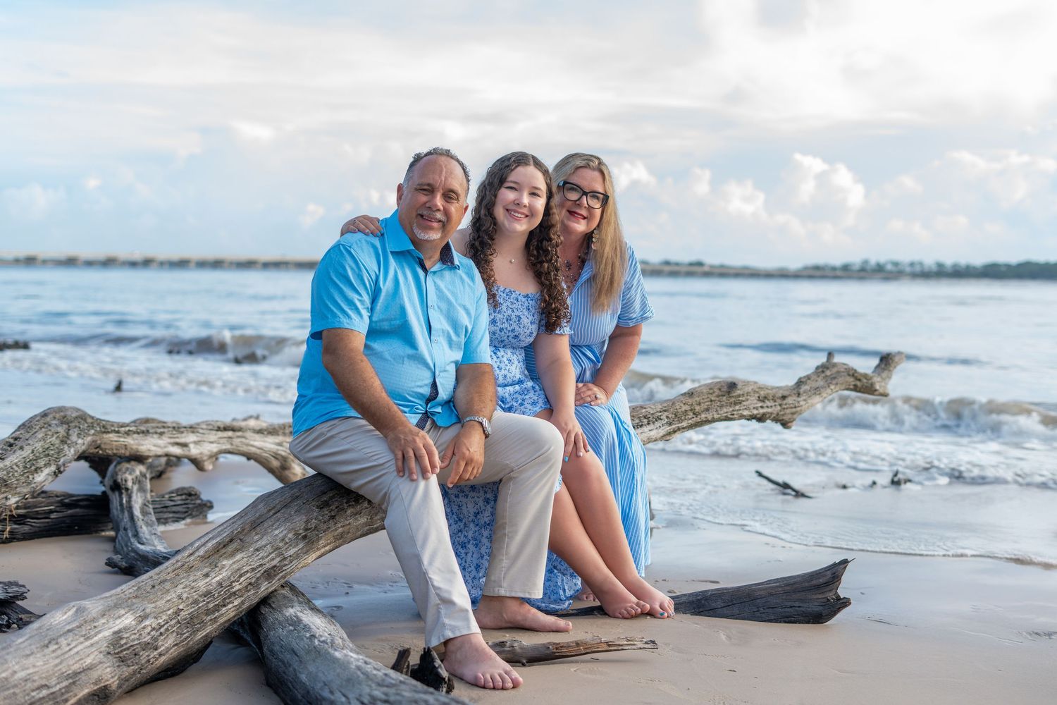 Family enjoying a sunny beach photo session with driftwood and waves in the background on a summer day.