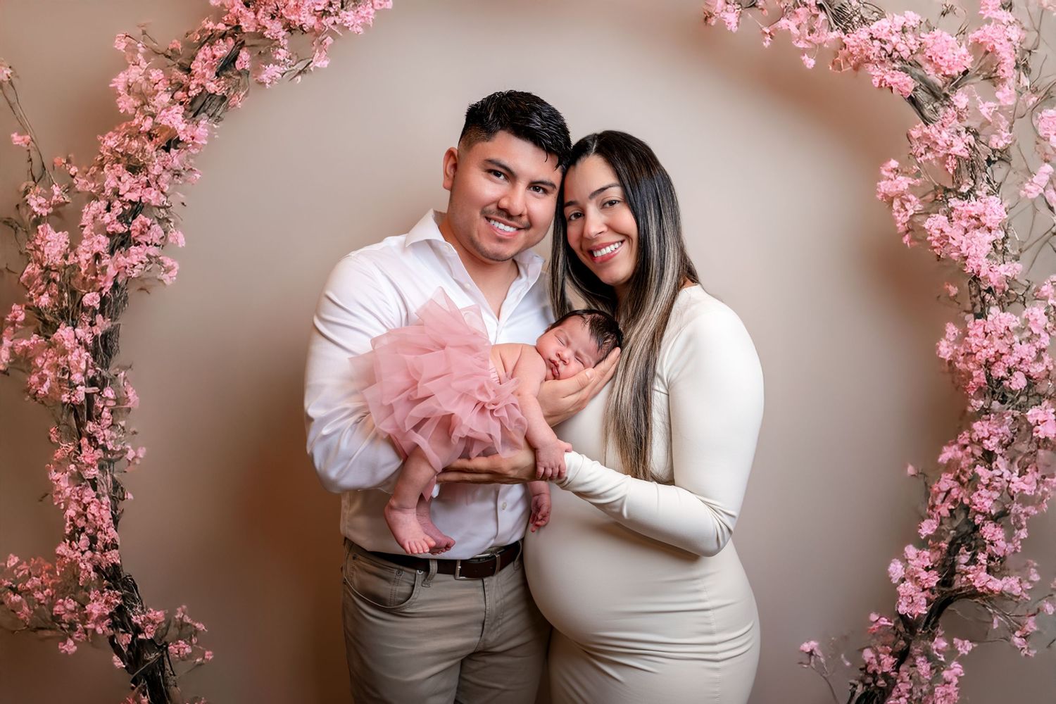 Family portrait session with pink cherry blossom decorations against a neutral wall backdrop.