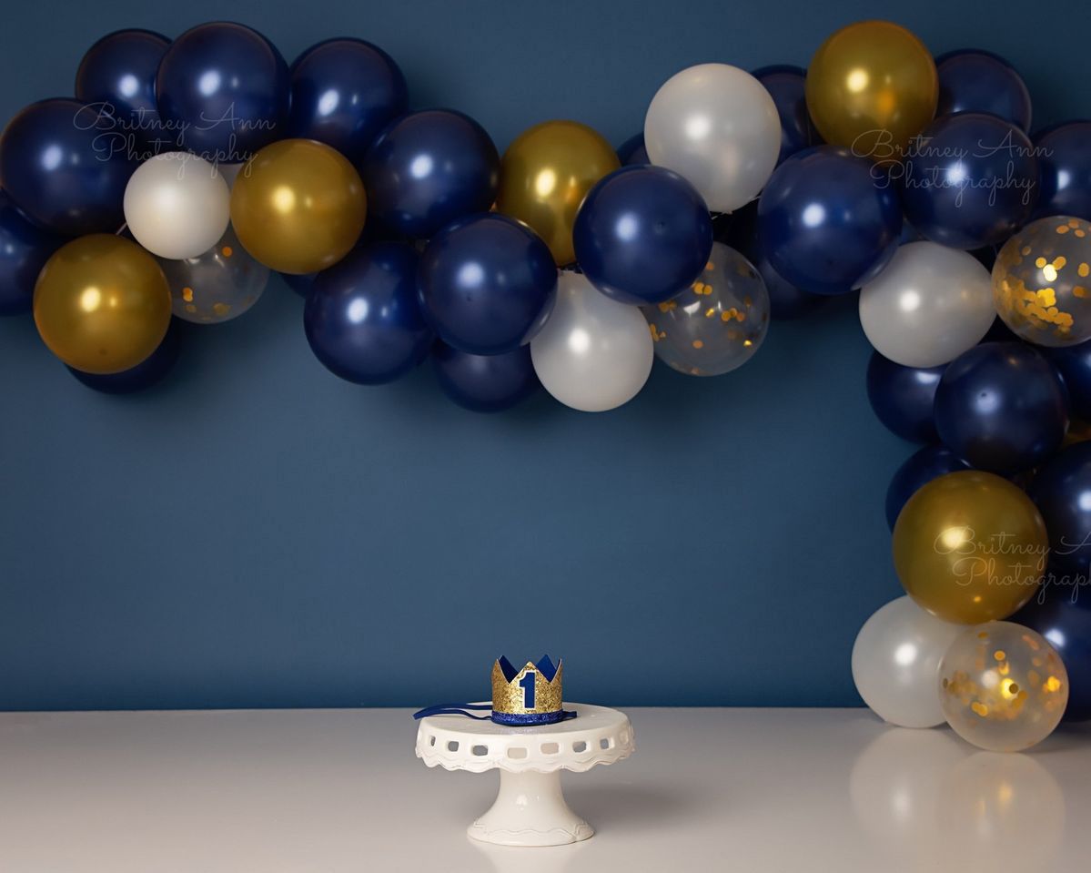 Navy blue and gold balloon garland arch decoration against a dark blue wall creating an elegant party backdrop.