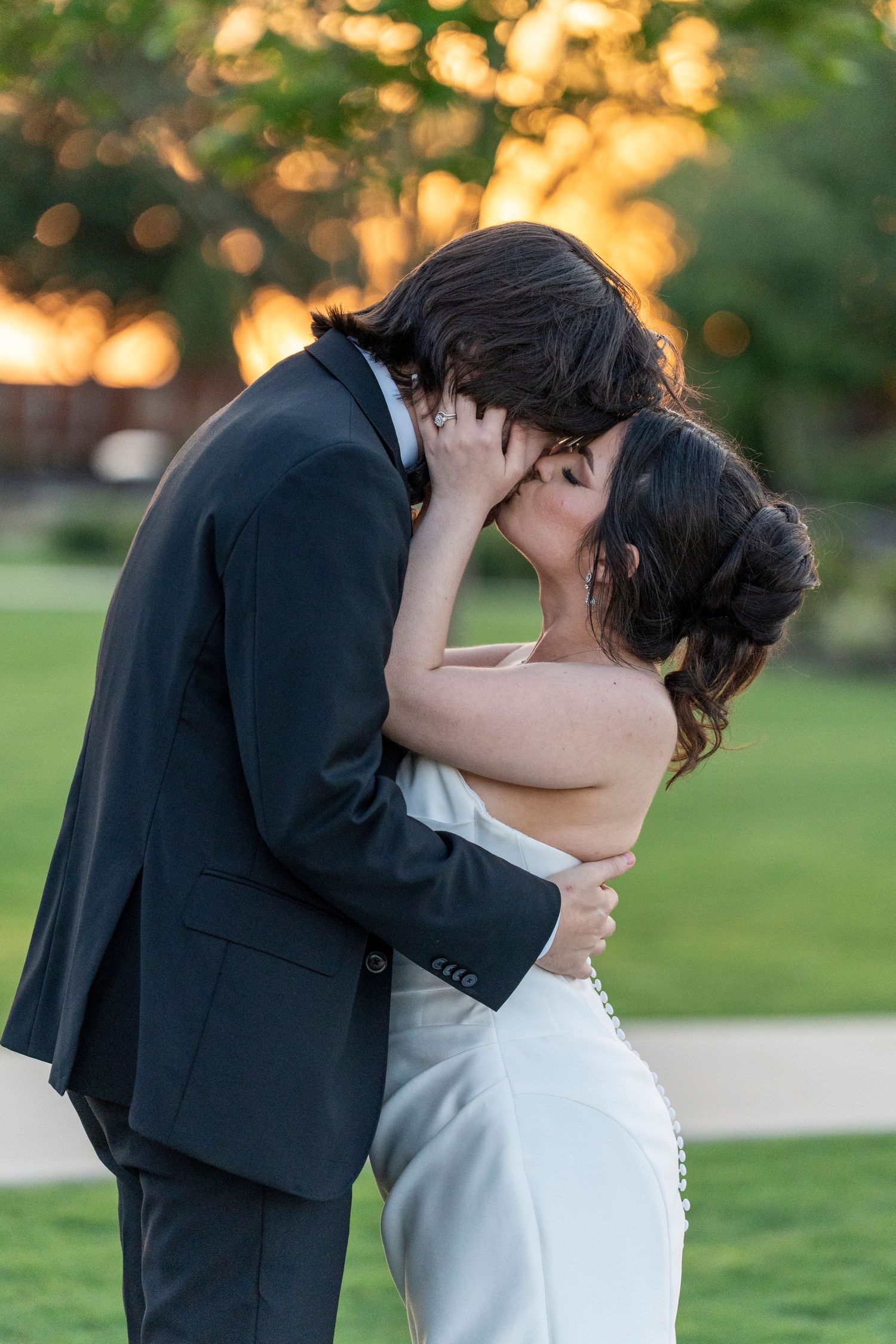 Bride and groom sharing romantic outdoor kiss at golden hour sunset.