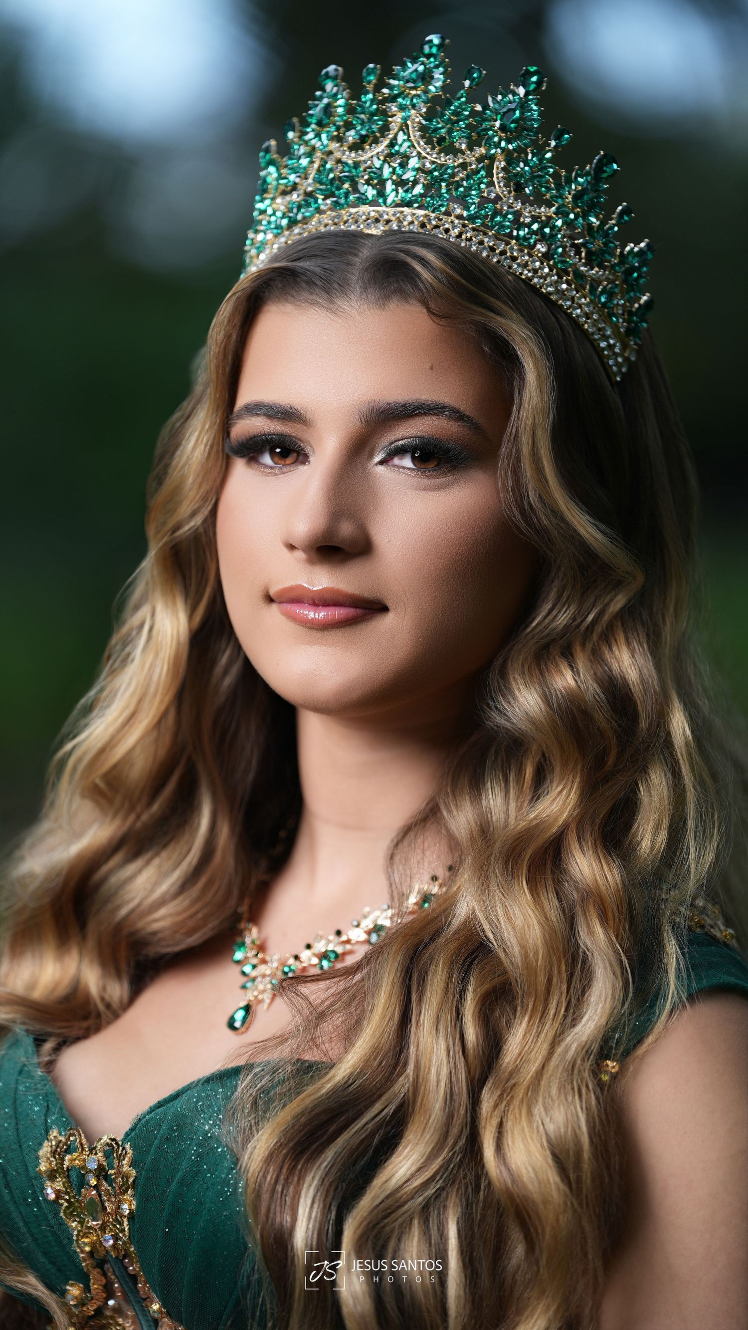Young woman wearing an emerald green crown and matching necklace with elegant wavy hair in a formal portrait.