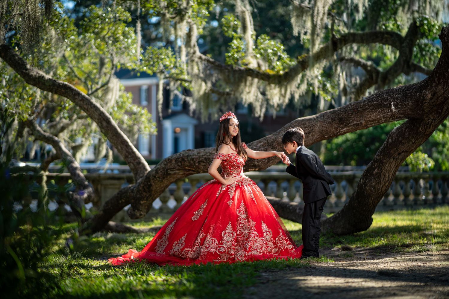 A couple in formal attire poses under Spanish moss-draped oak trees in a romantic garden setting.