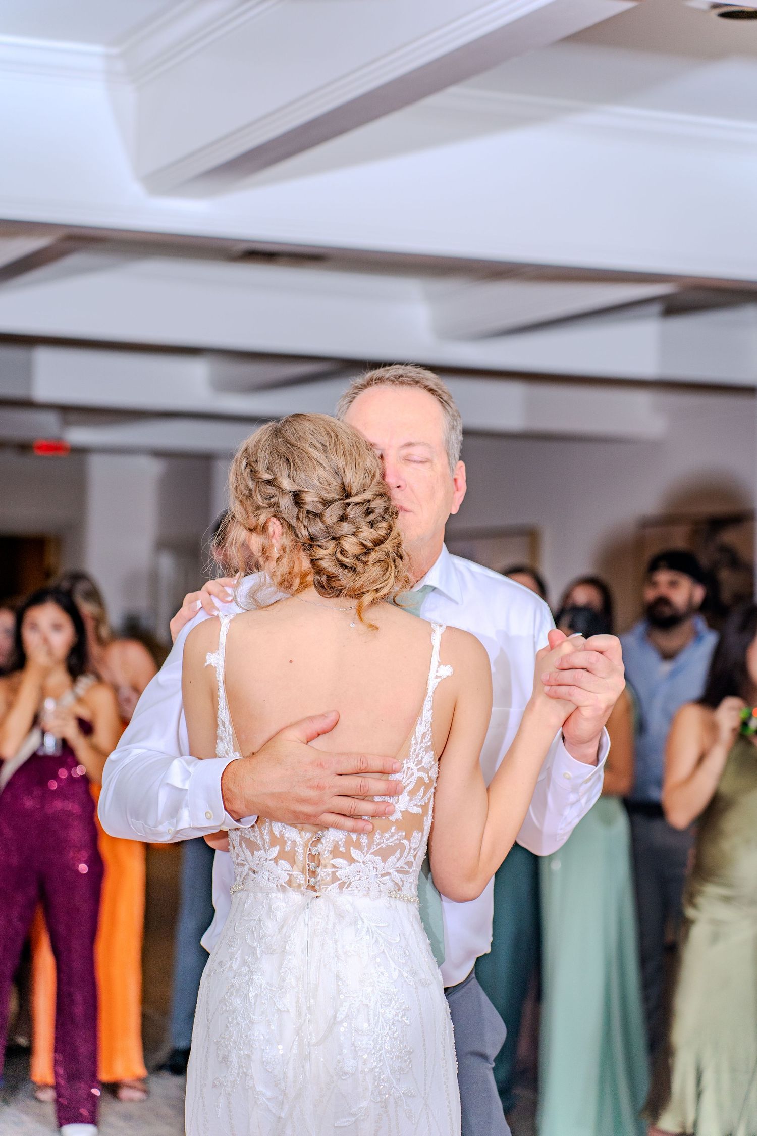 Emotional wedding dance sequence showing couple embracing while wedding guests watch in background.