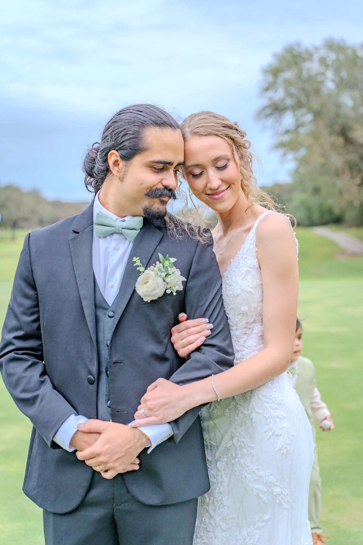 A wedding couple shares an intimate embrace outdoors in a lush green field on their special day.