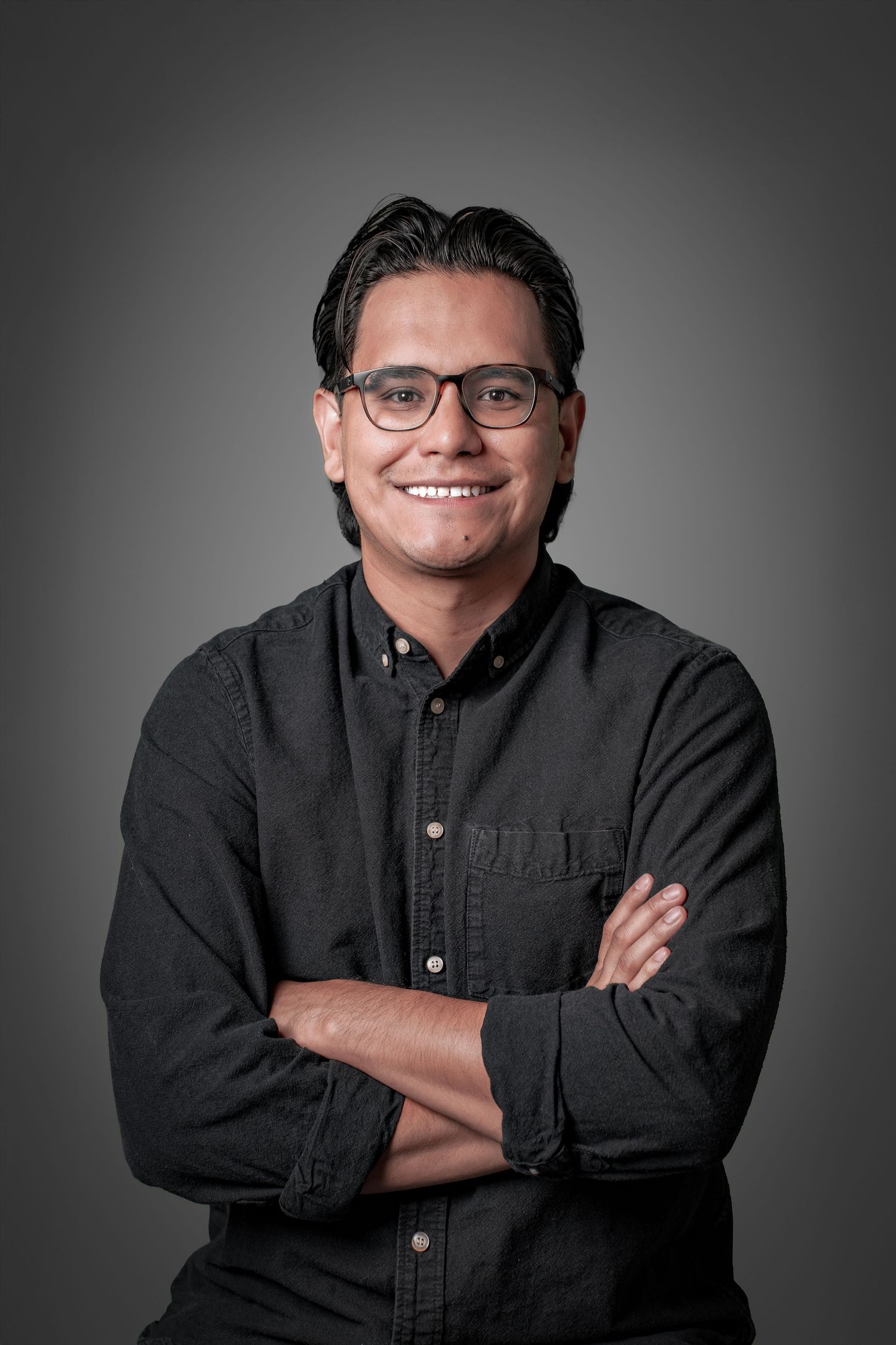 Professional studio portrait of a person in glasses and dark button-down shirt against gray background.