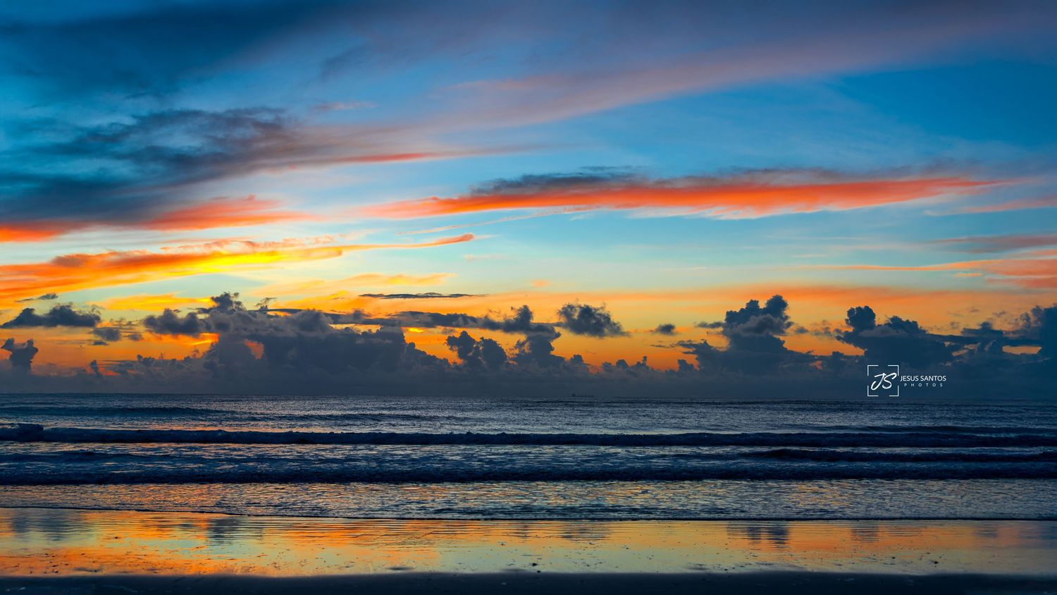 Panoramic seascape of dramatic colorful sunset over ocean horizon with vibrant clouds reflecting in calm waters.