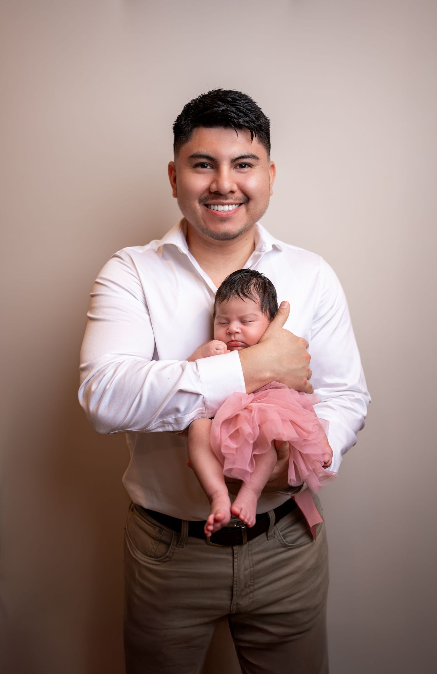 Studio photo series showing a baby in a pink tulle outfit being held against a neutral backdrop.