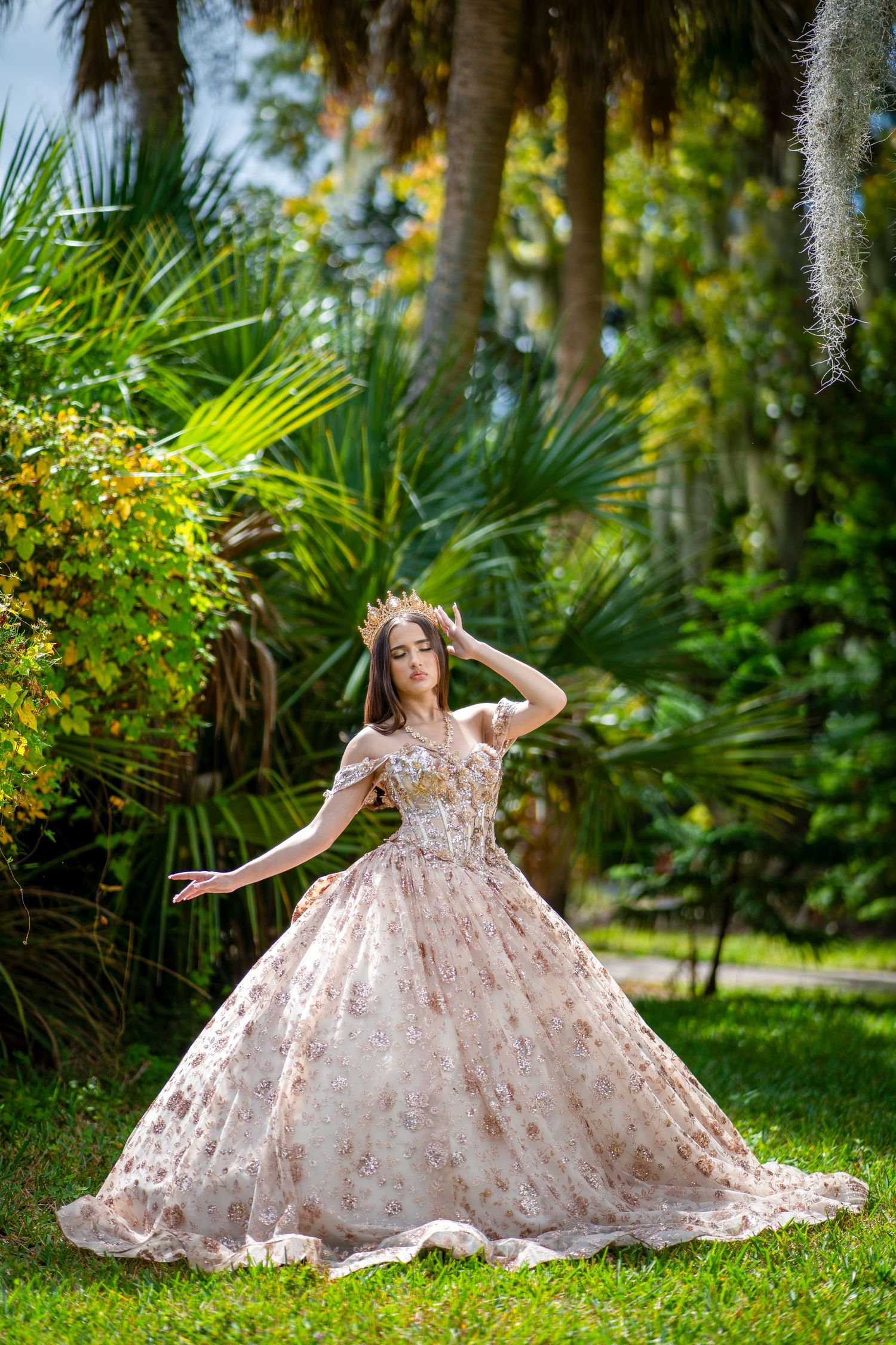 A flowing floral ballgown dress twirls gracefully in a lush tropical garden setting with palm trees and greenery.