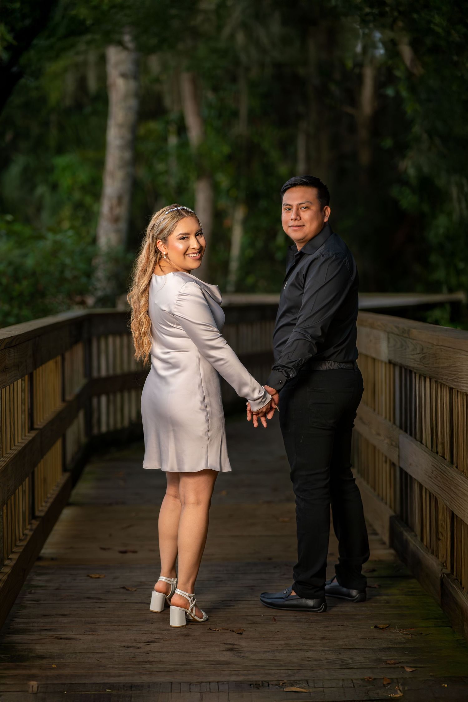 Romantic engagement photo session on a wooden boardwalk surrounded by lush green forest.