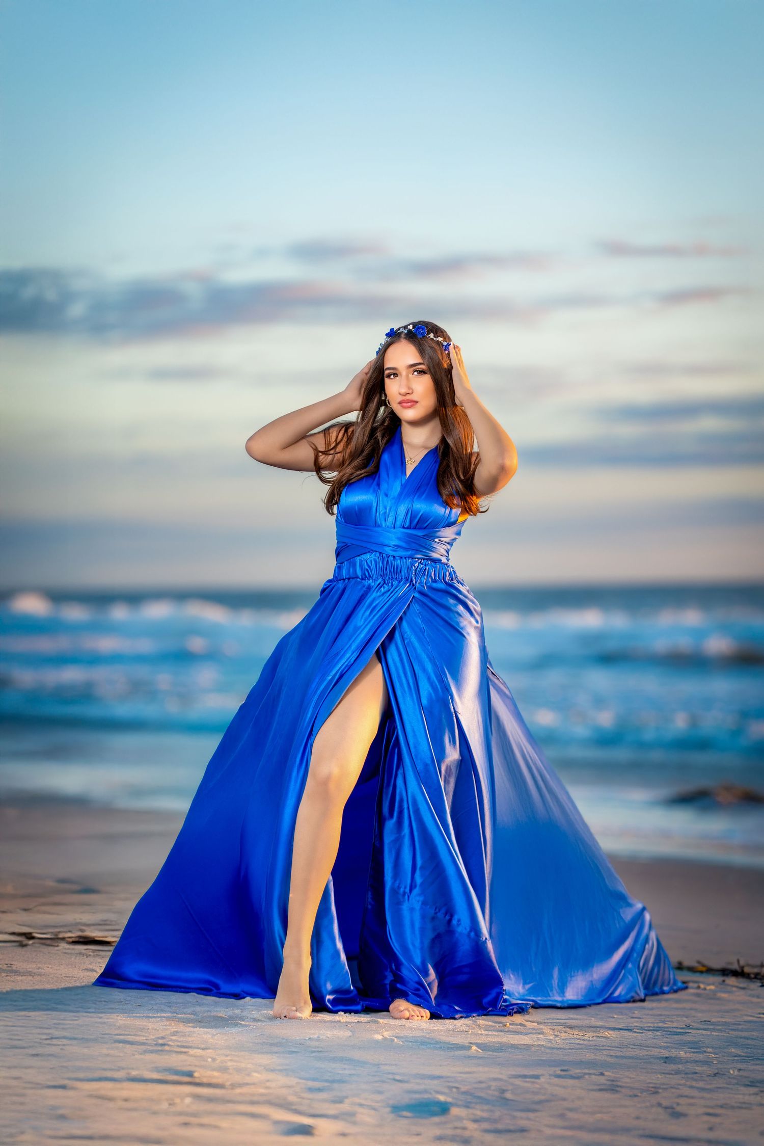 Flowing royal blue evening gown with thigh-high slit photographed on beach at sunset.