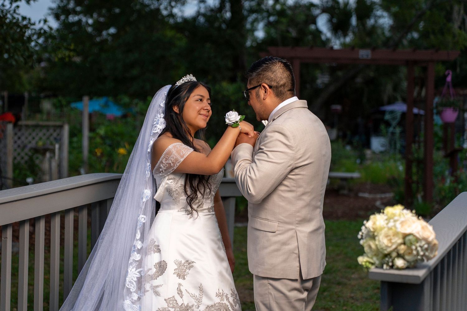 Bride pins boutonniere on groom's lapel on wooden deck during romantic outdoor wedding ceremony.