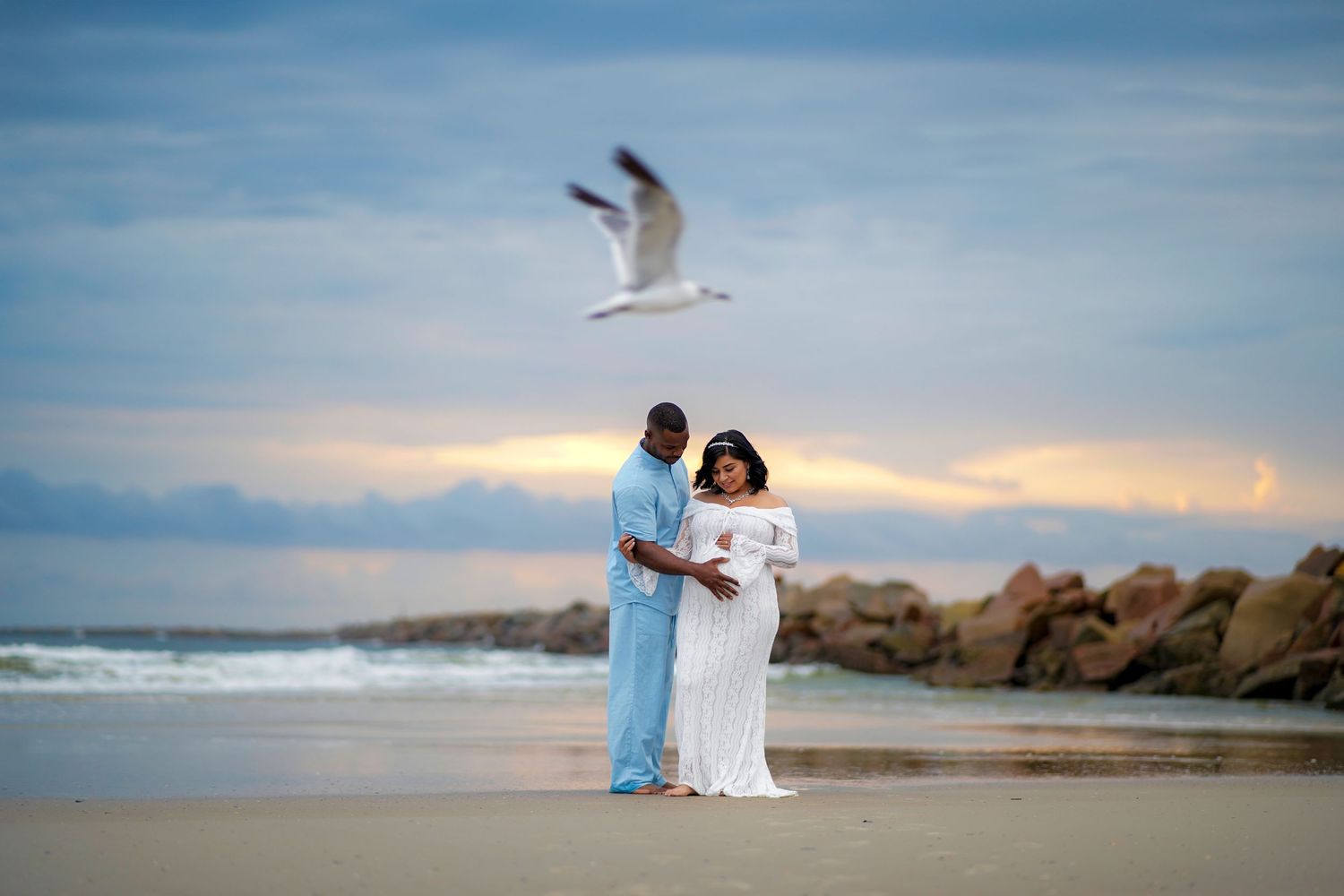 A coastal wedding photography session shows a couple walking along a rocky beach at sunset with waves crashing nearby.