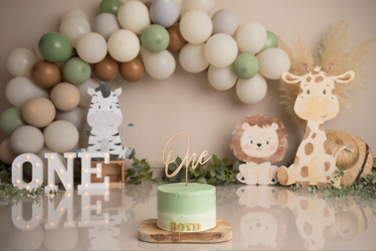 Safari themed first birthday party setup with balloon arch, animal cutouts, and mint green cake on display table.