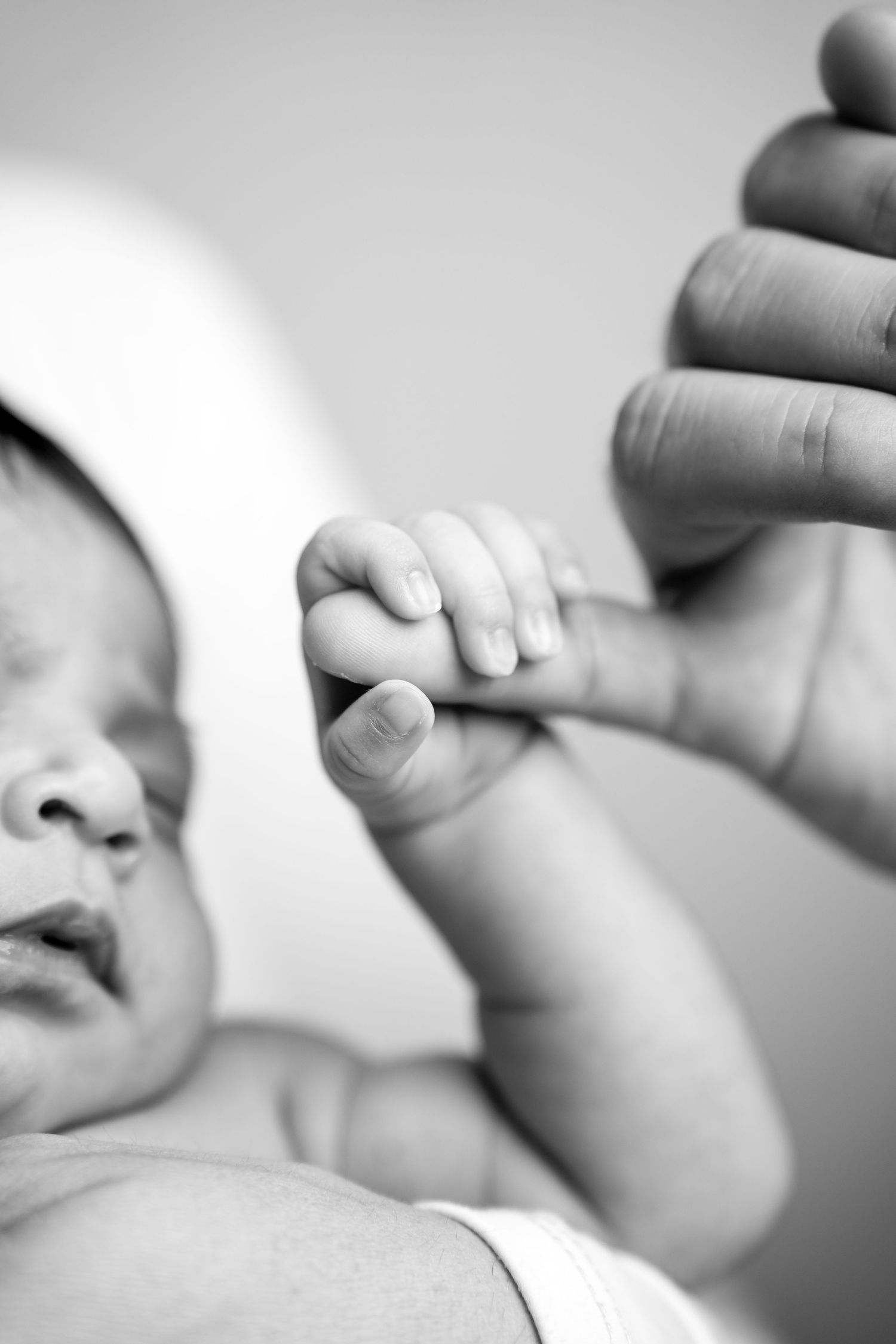 A tiny baby's hand grasps an adult finger while sleeping in black and white.