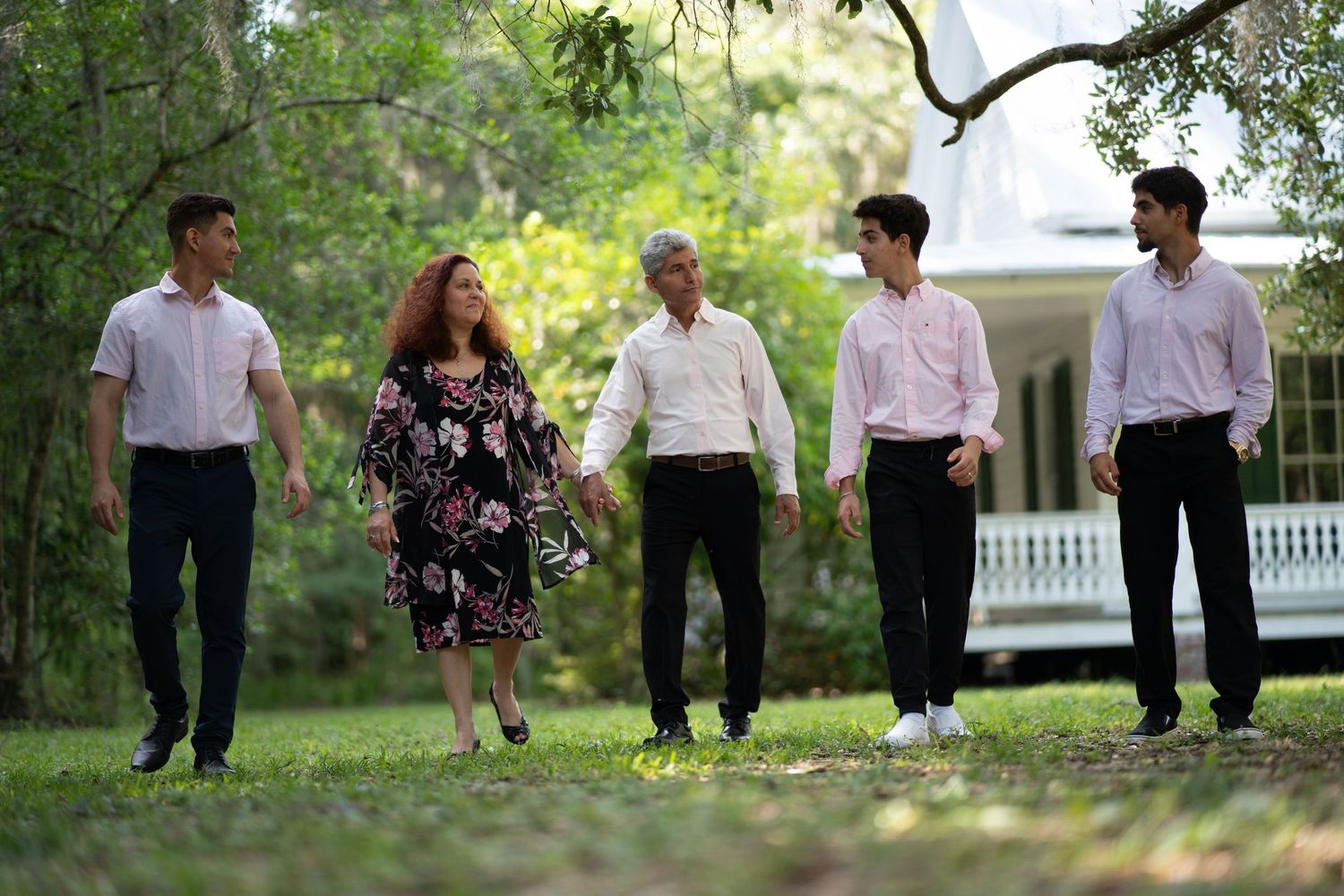 Group walking along a wooded path in casual semi-formal attire during a sunny day outdoors.