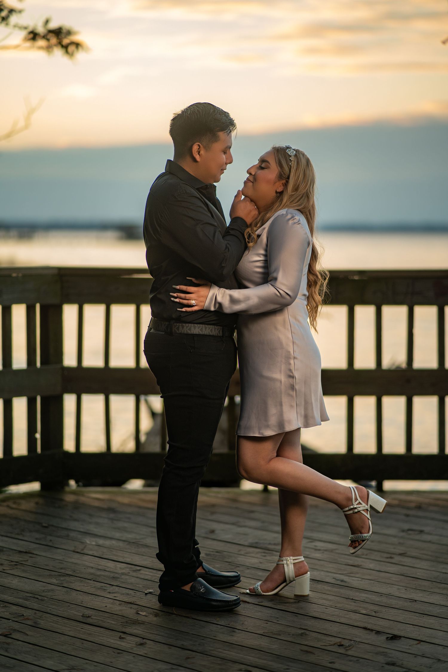 Two young children in formal attire share a sweet moment on a wooden pier at sunset.