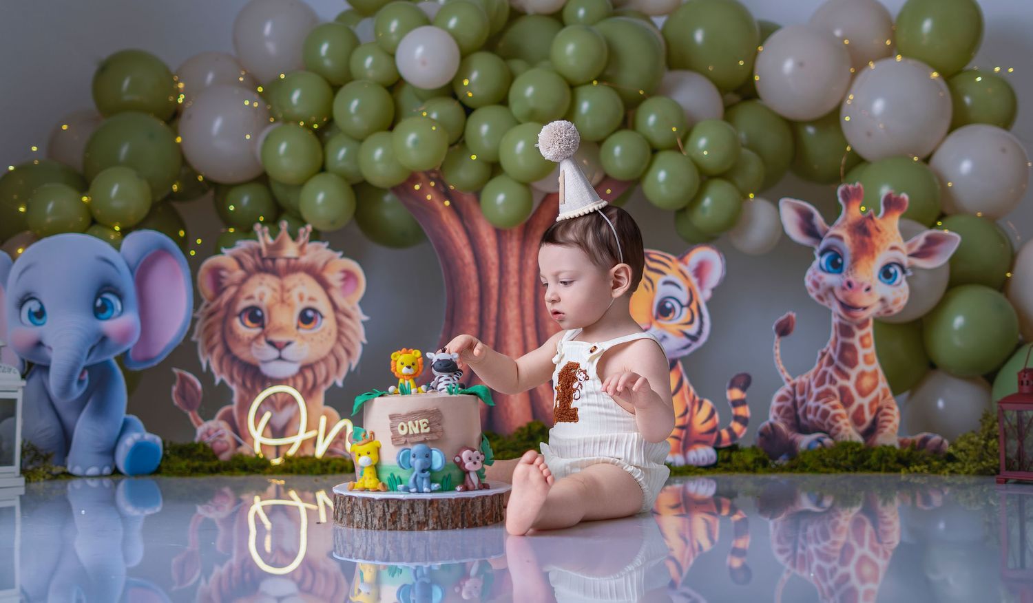 Baby's first birthday jungle safari cake smash with lion, elephant, and giraffe cutouts and green balloon arch.