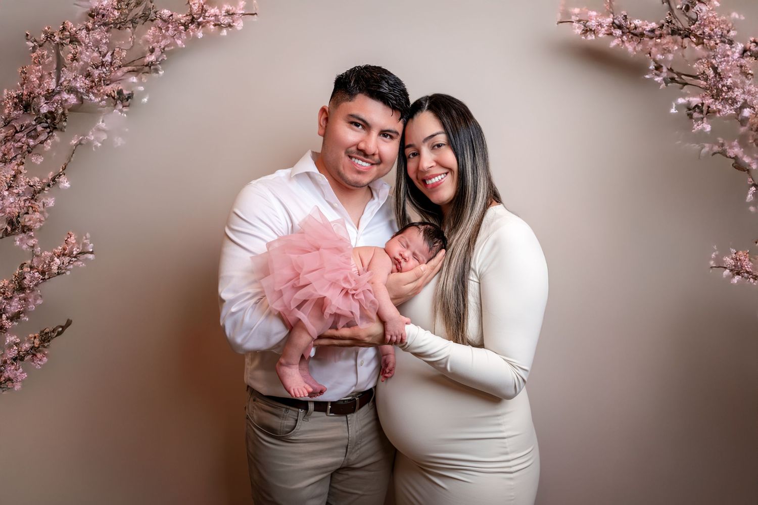 A couple poses with pink cherry blossoms for romantic pregnancy announcement photos in a studio setting.