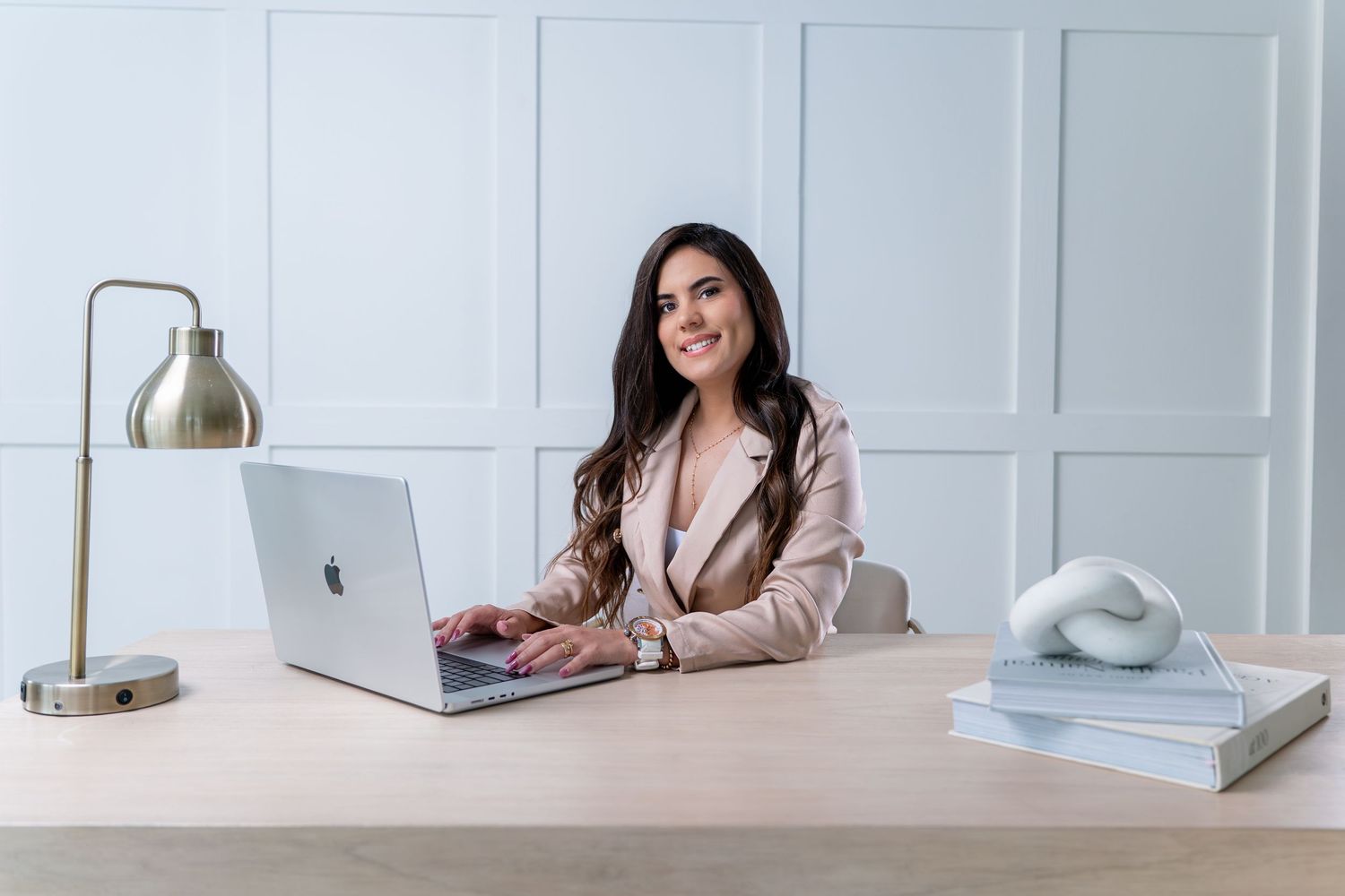 Professional working at desk with laptop computer and gold desk lamp in modern white office setting.