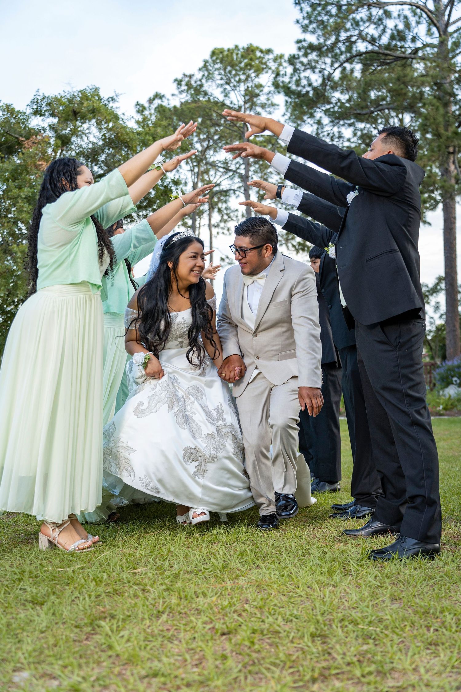 Bride and groom walk through an arch of raised hands formed by wedding party guests outdoors.