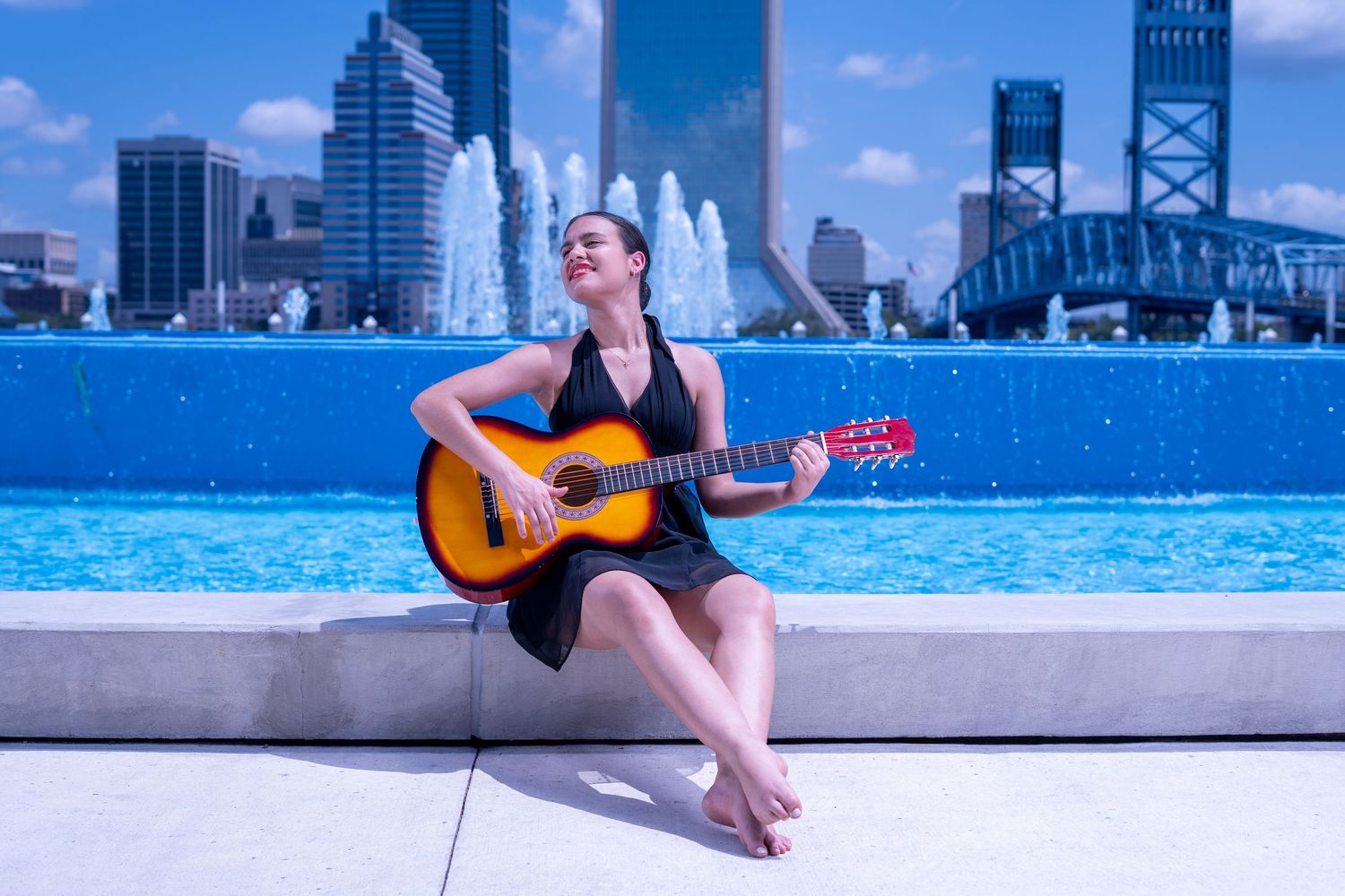 A musician performing with an acoustic guitar at a rooftop pool with Jacksonville's skyline in the background.