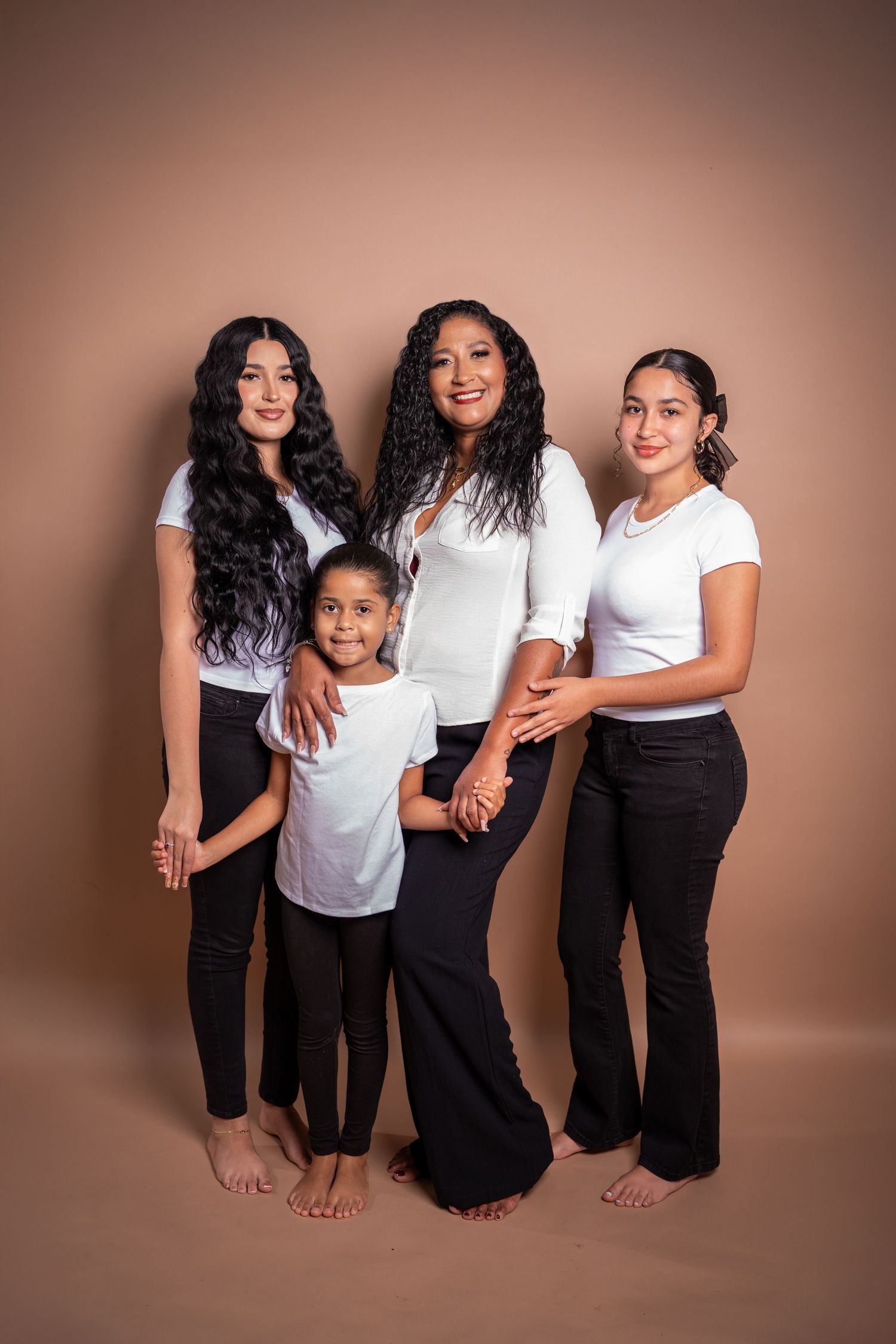 A family in matching white tops and black pants poses in front of a brown background in five progressive shots.