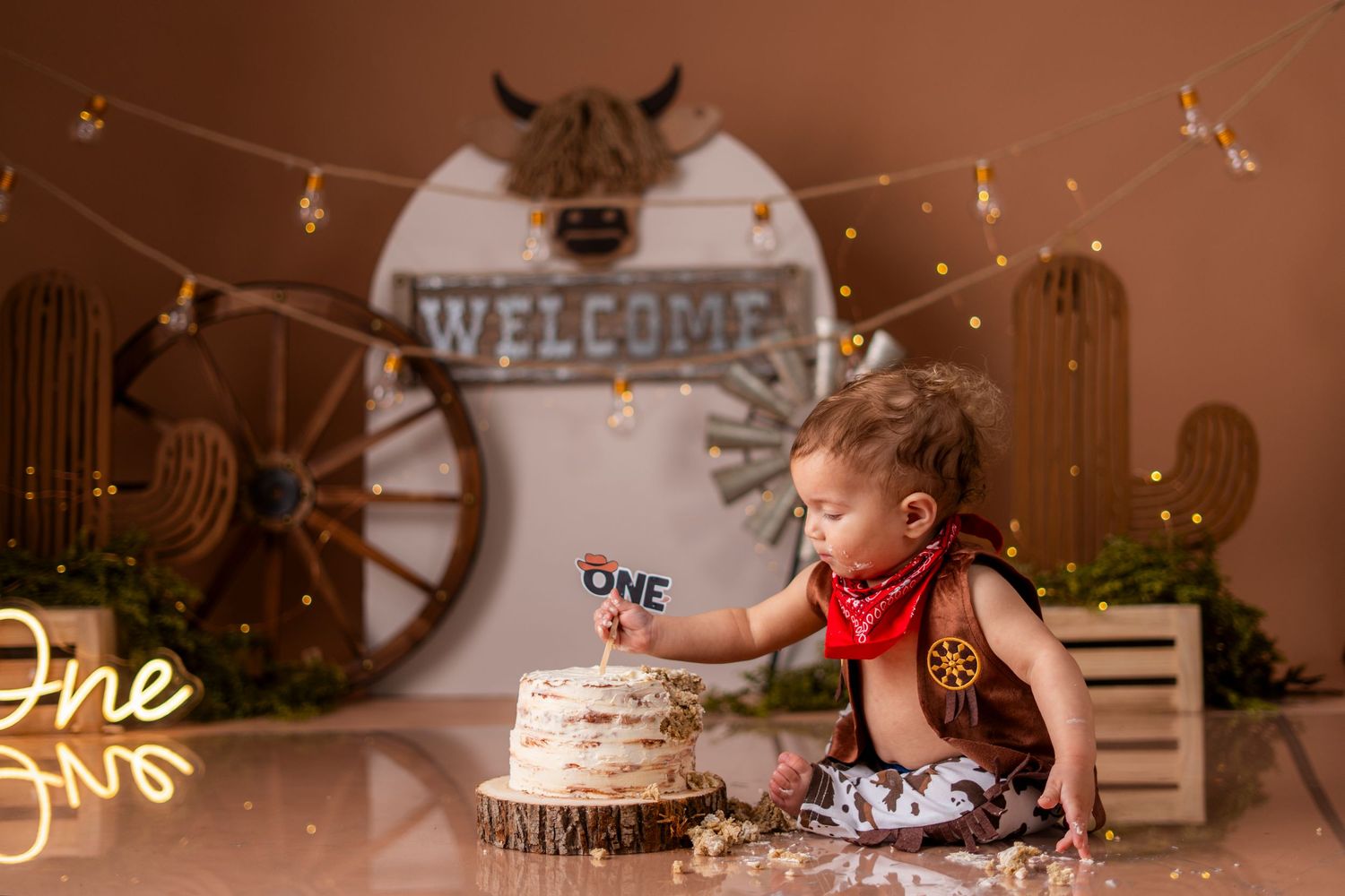 A festive first birthday party scene with twinkle lights, wooden decor, and rustic welcome signage.