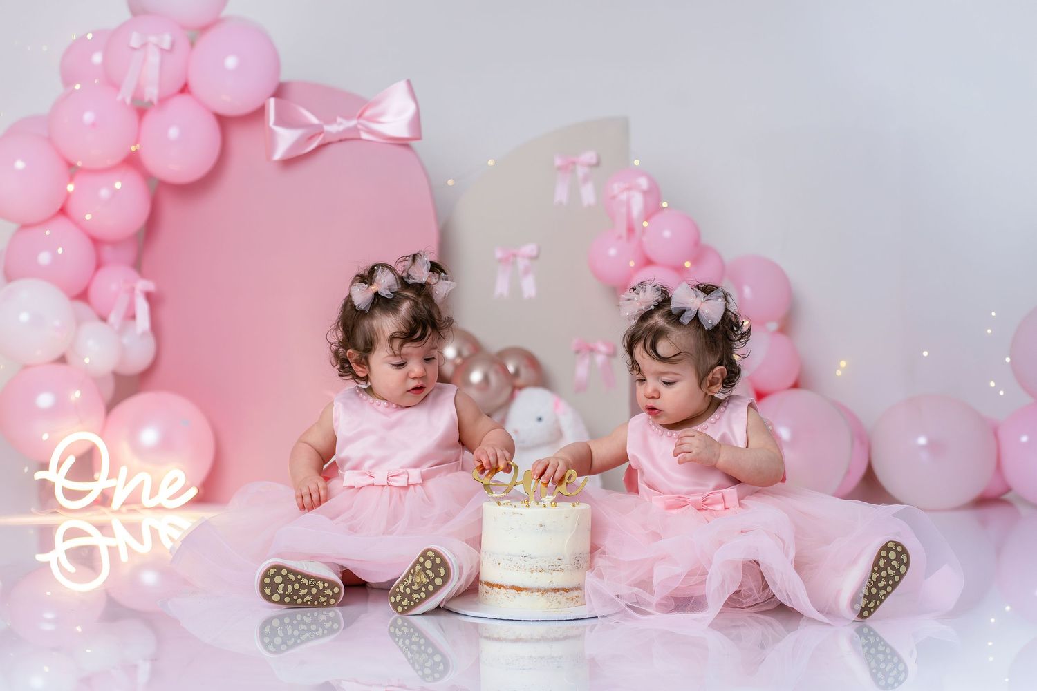 Pink balloon arch with neon lights and white cake display creates a romantic party atmosphere.