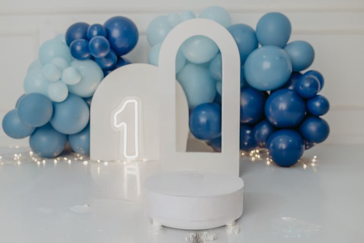 Navy blue and white balloon garland decorates a party space with a cloud-themed backdrop and white seating area.