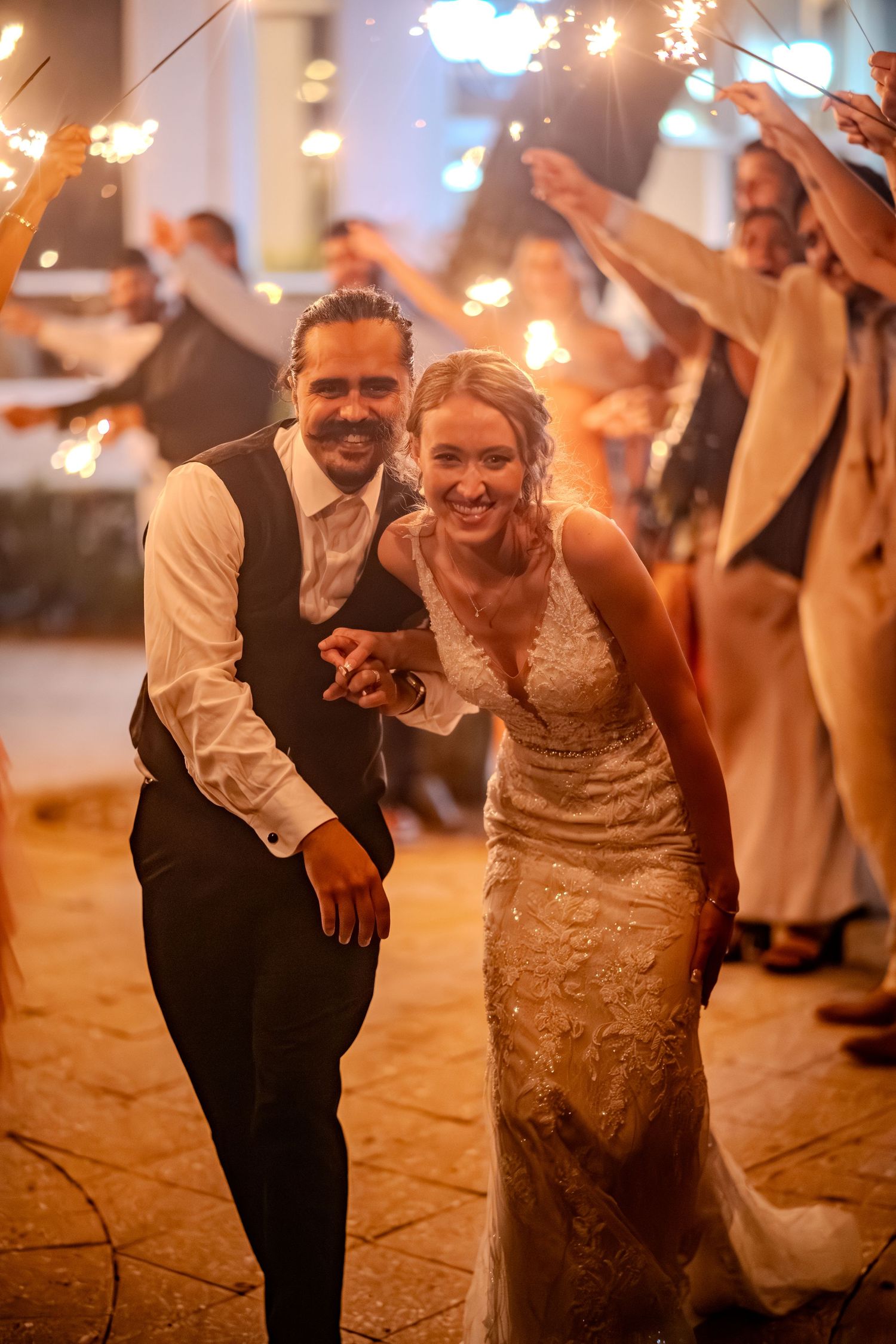 Newlywed couple runs through sparkler tunnel at evening wedding reception exit celebration.