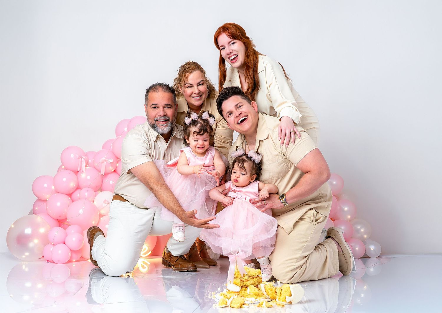 A group poses together in a studio setting with pink balloons and yellow flowers against a white backdrop.
