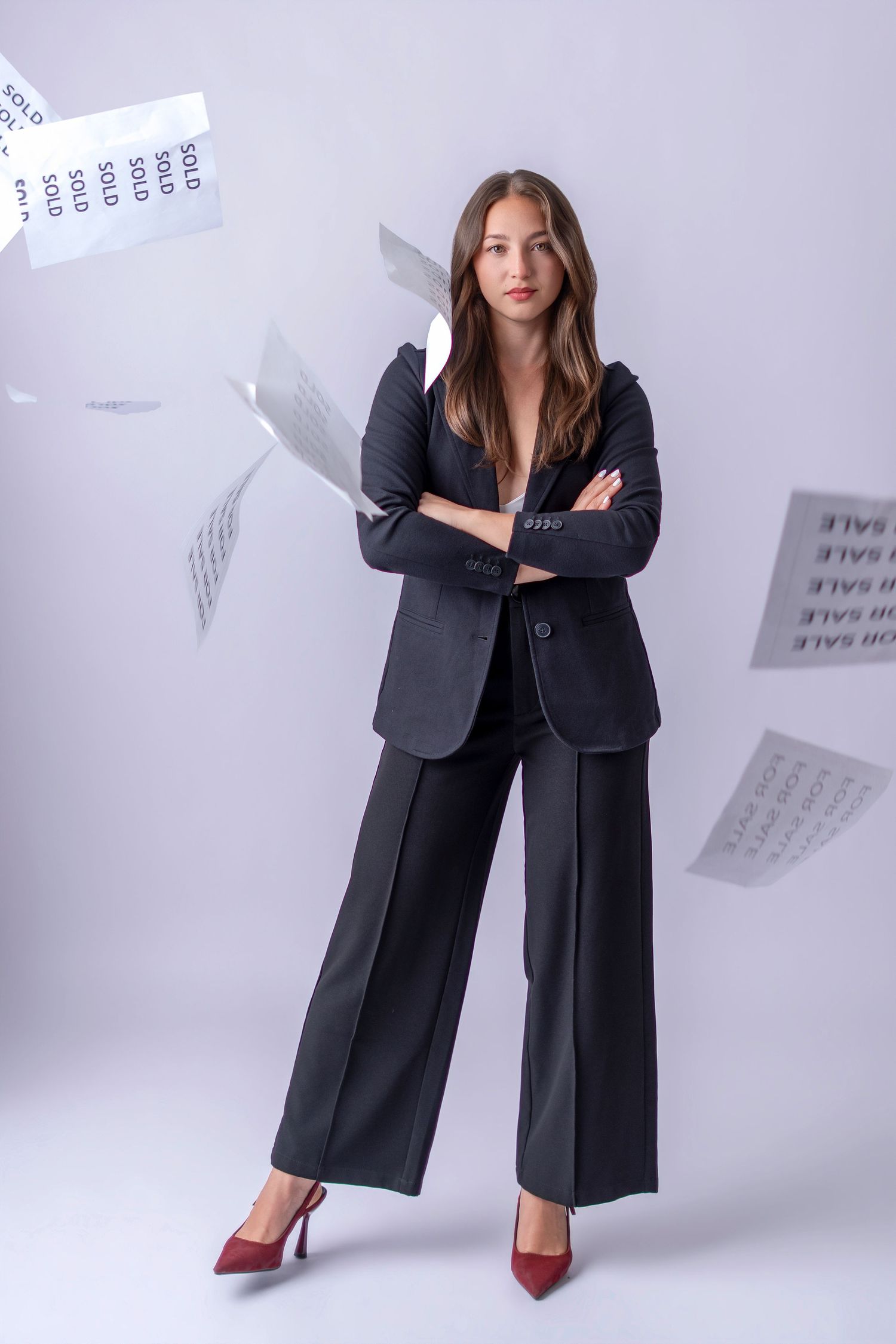 Professional woman in black pantsuit with crossed arms, surrounded by flying sold signs and papers on white background.