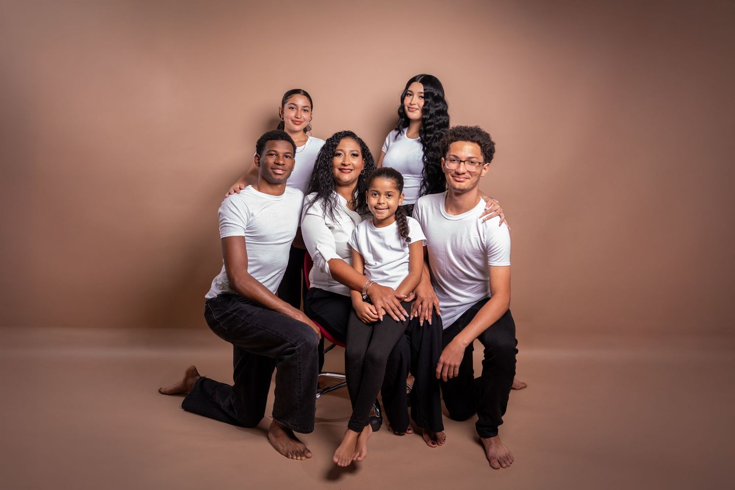 A group of people wearing white and black outfits pose together for a studio portrait against a brown backdrop.