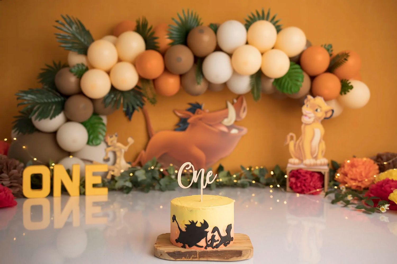 Elegant party decor with white balloons, greenery garland, and pink flowers against an orange-tinted wall.