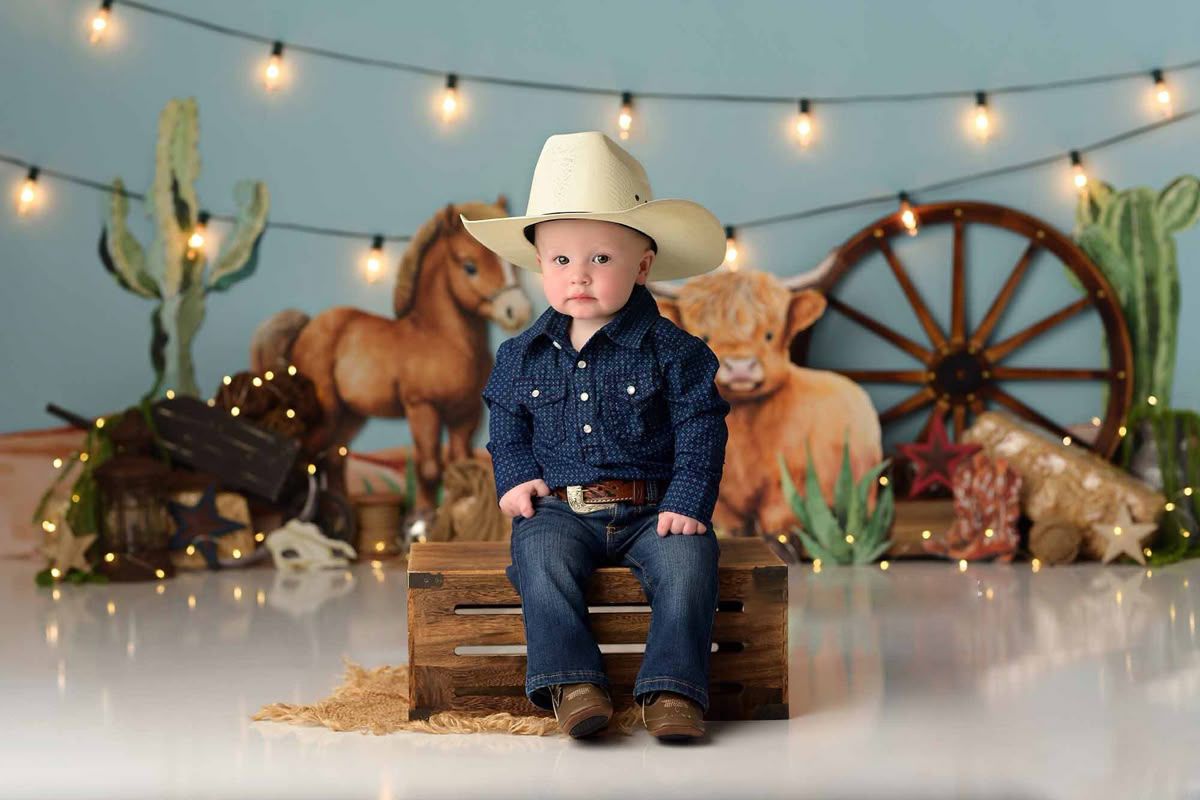 Western-themed birthday party setup with string lights, wagon wheel decor, and rustic elements against a neutral backdrop.