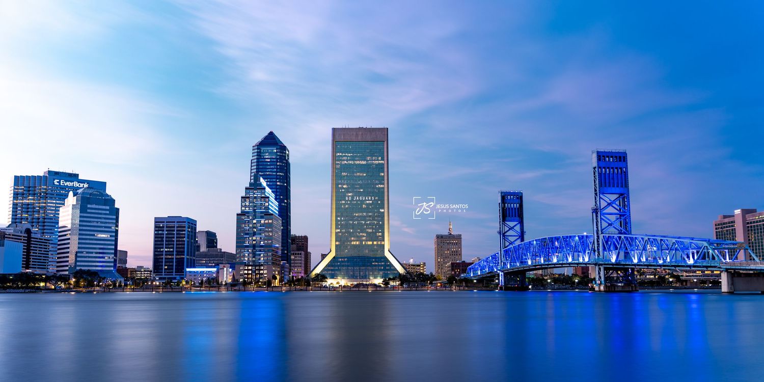 Jacksonville Florida skyline panorama reflects in St Johns River during sunset with blue sky and clouds.