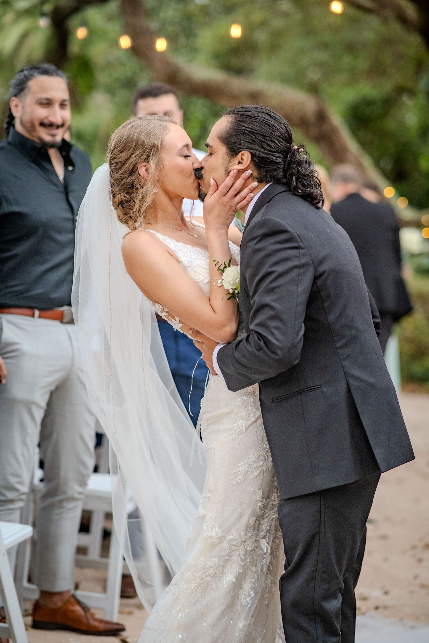 A romantic wedding ceremony moment outdoors with string lights and trees in the background.