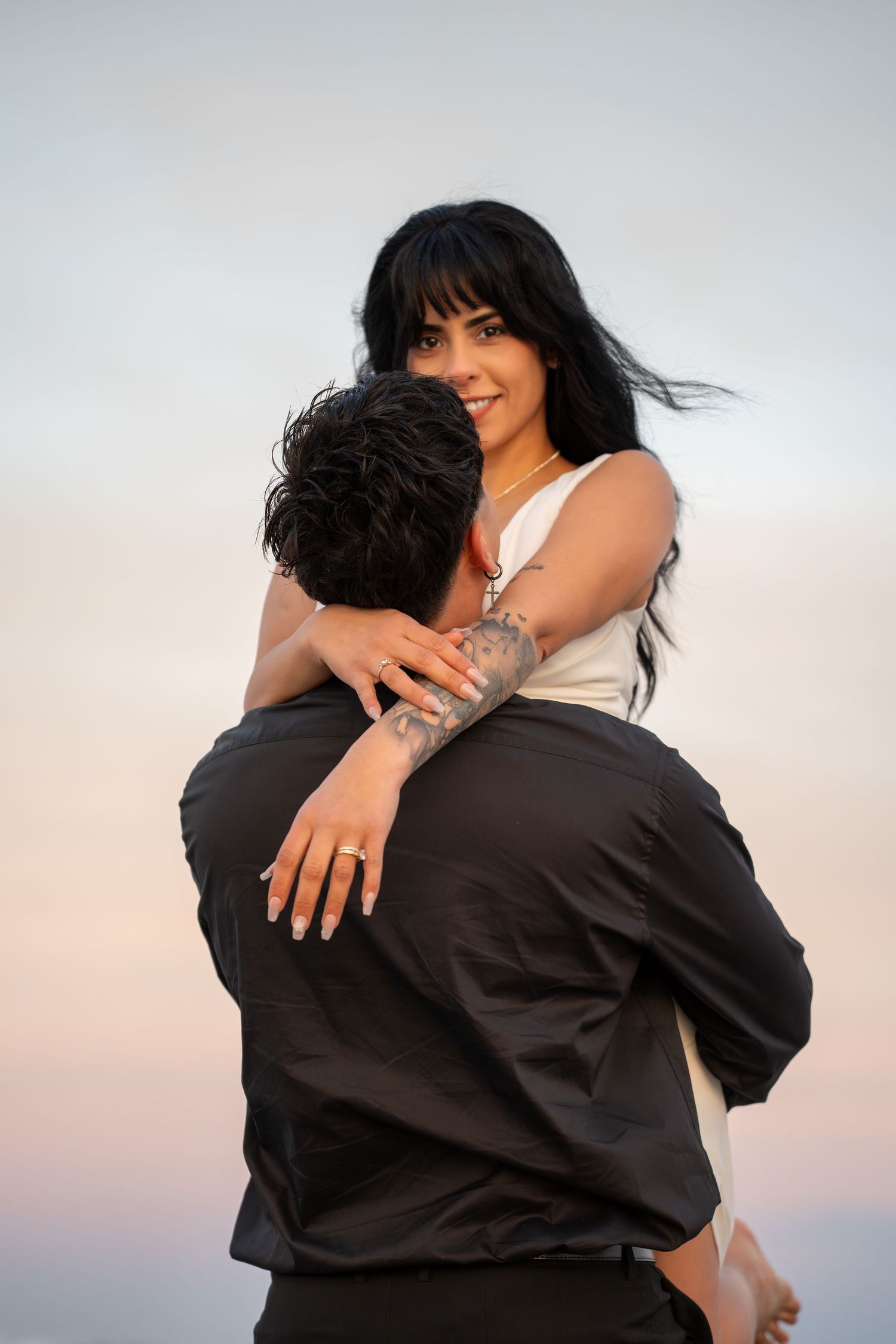 A couple in embrace wearing contrasting black and white outfits against a soft sky background.