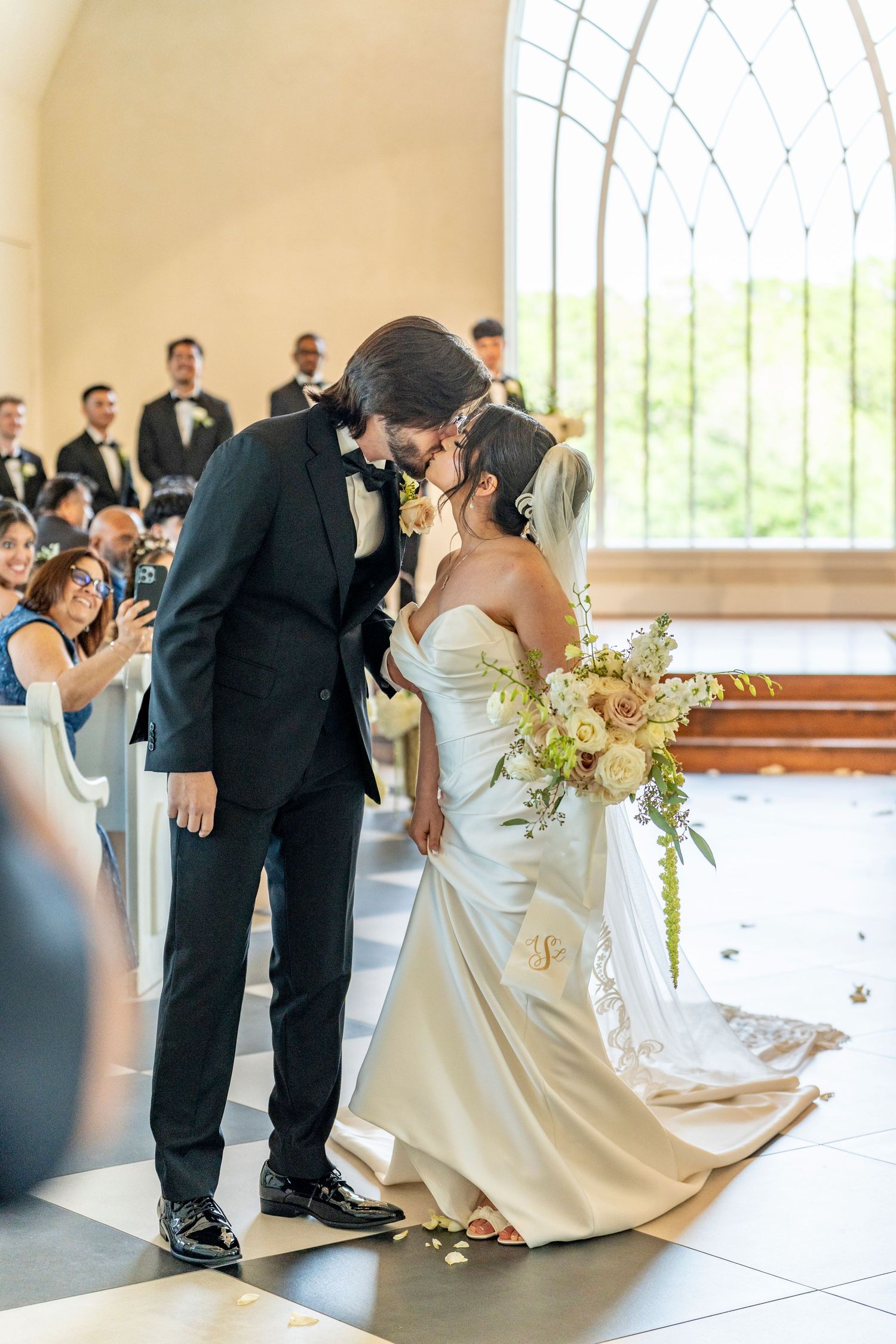 Bride and groom sharing first kiss at chapel altar with guests celebrating.