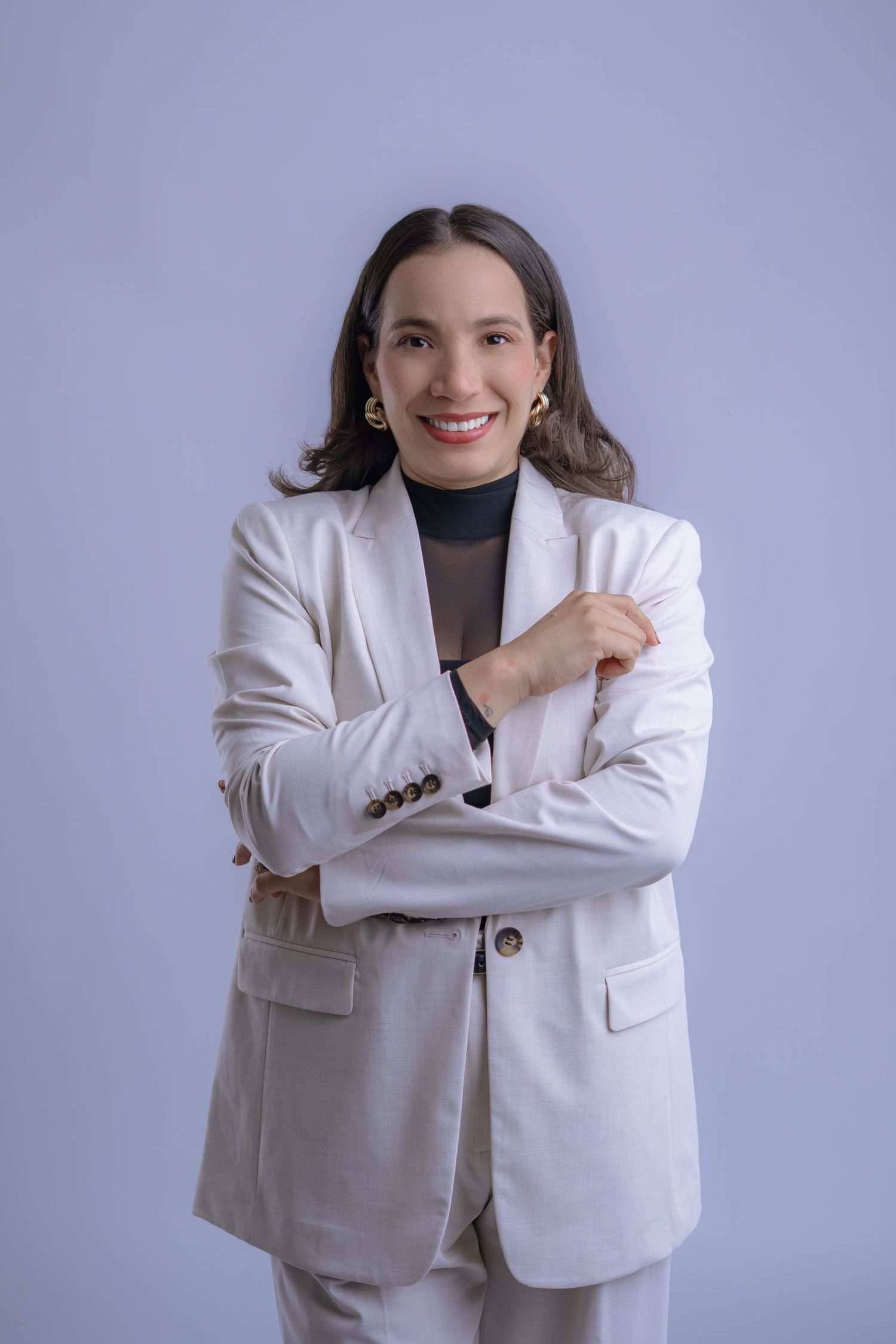 Smiling woman in white blazer suit with arms crossed against light blue background, professional business portrait.