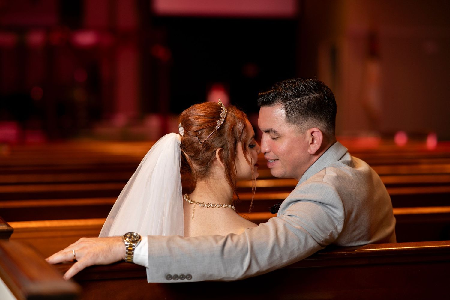 A romantic couple shares an intimate moment while sitting together in a church pew.