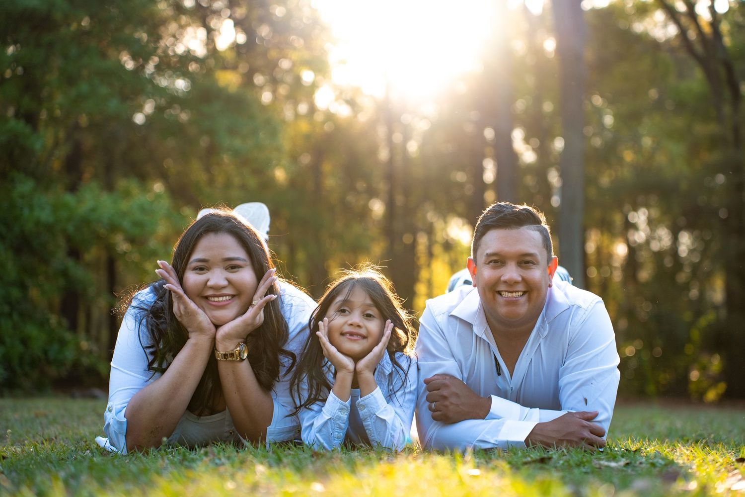 A happy family lying in the grass during golden hour, photographed from different angles in outdoor portraits.