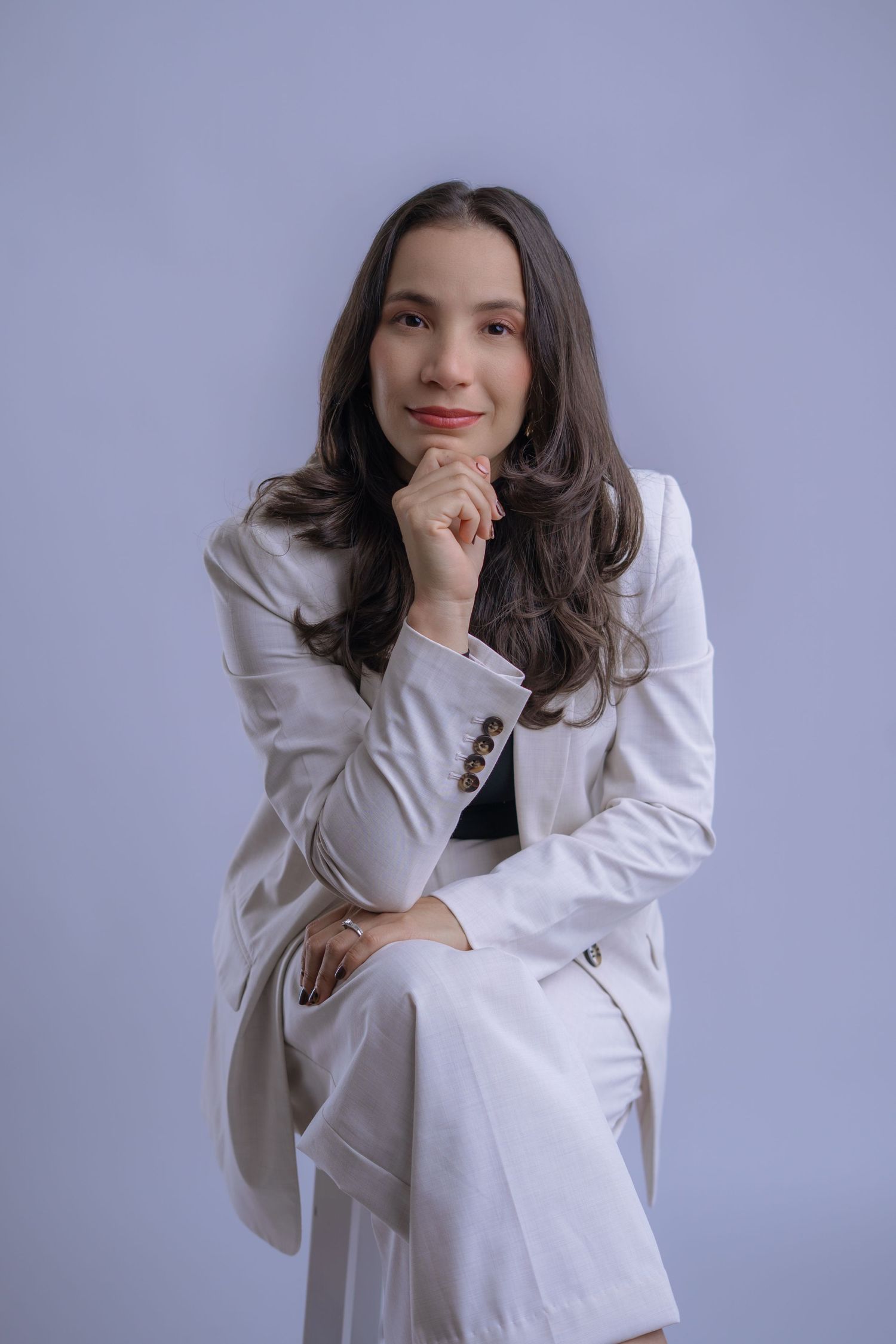 A person in a white blazer poses against a gray background with natural lighting and relaxed expressions.