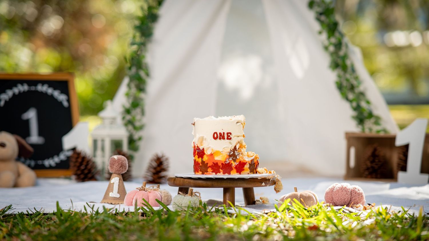 A table setting at an outdoor wedding reception with white linens and floral centerpieces under a canopy of trees.