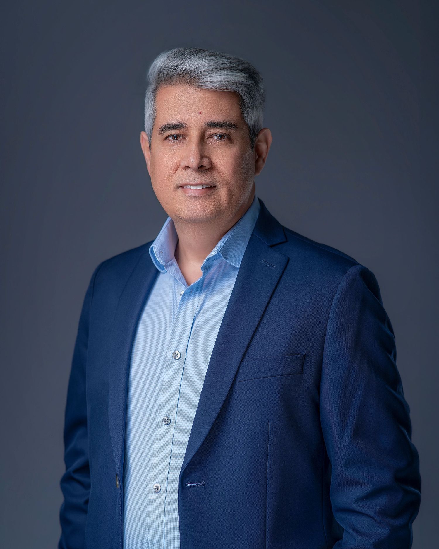 Professional headshot of a confident middle-aged man with gray hair wearing a blue blazer and light blue shirt.