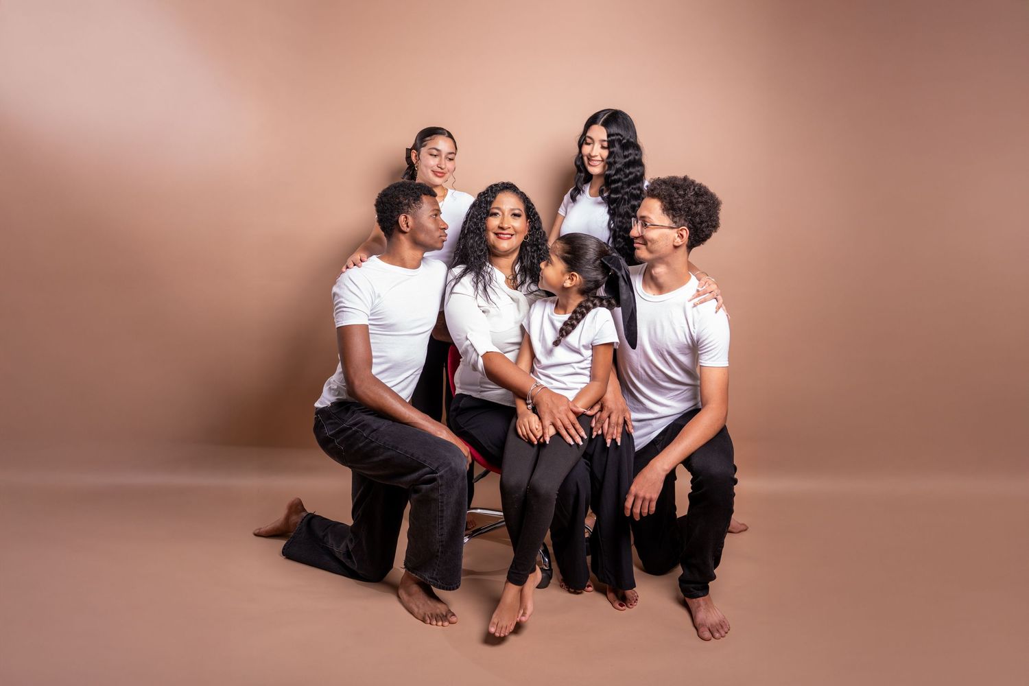 Happy group of people in white shirts lounging and laughing together against warm brown studio backdrop.