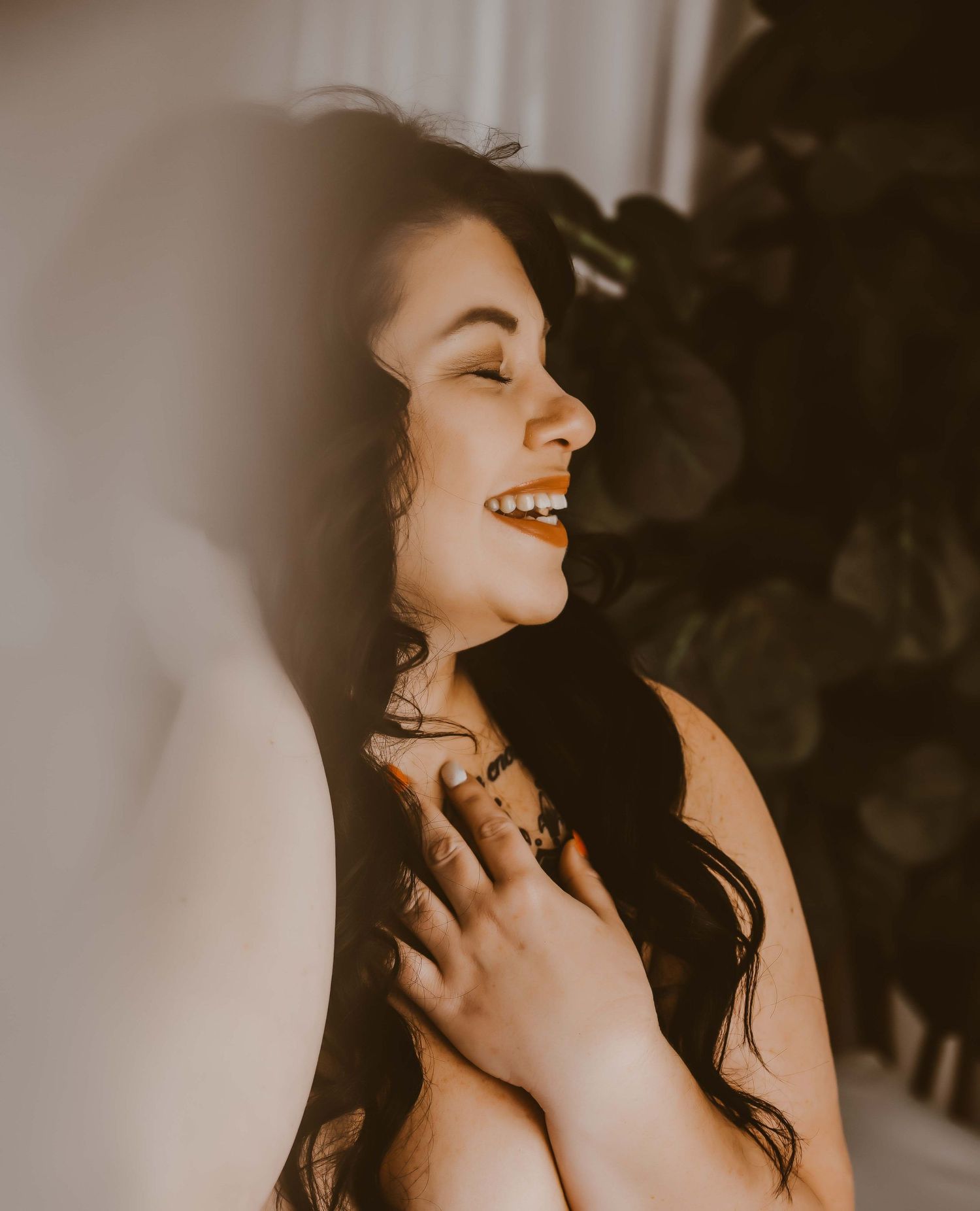 Boudoir portrait – joyful woman with eyes closed, laughing and radiant.