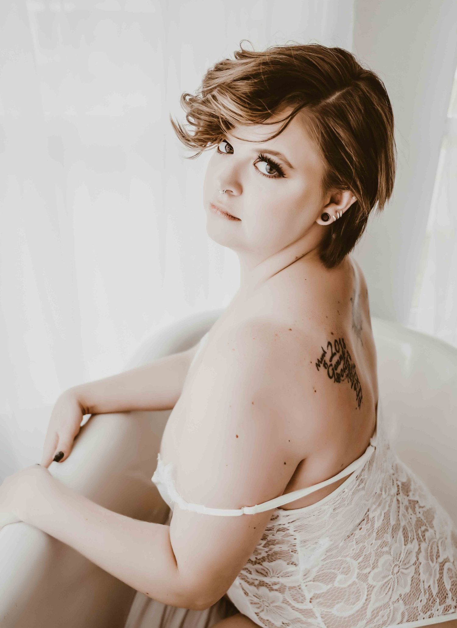 White lace boudoir photography – Short-haired woman with back tattoo, posing in white lace lingerie in bright natural light.