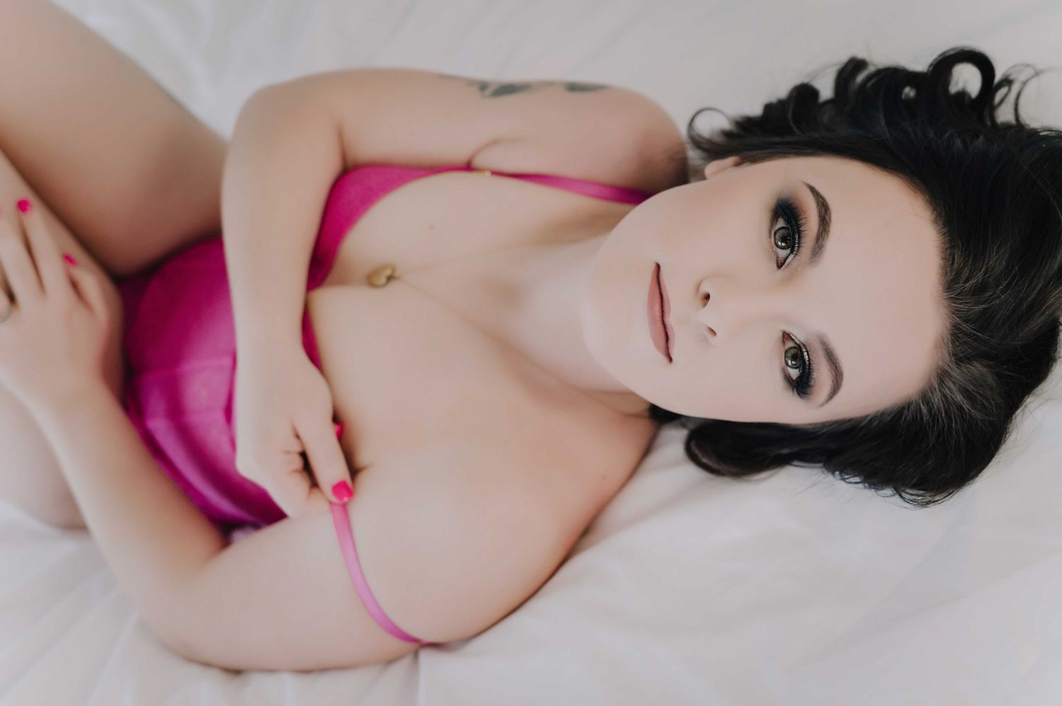 Empowering boudoir portrait – woman in pink lingerie on bed, playful and confident.