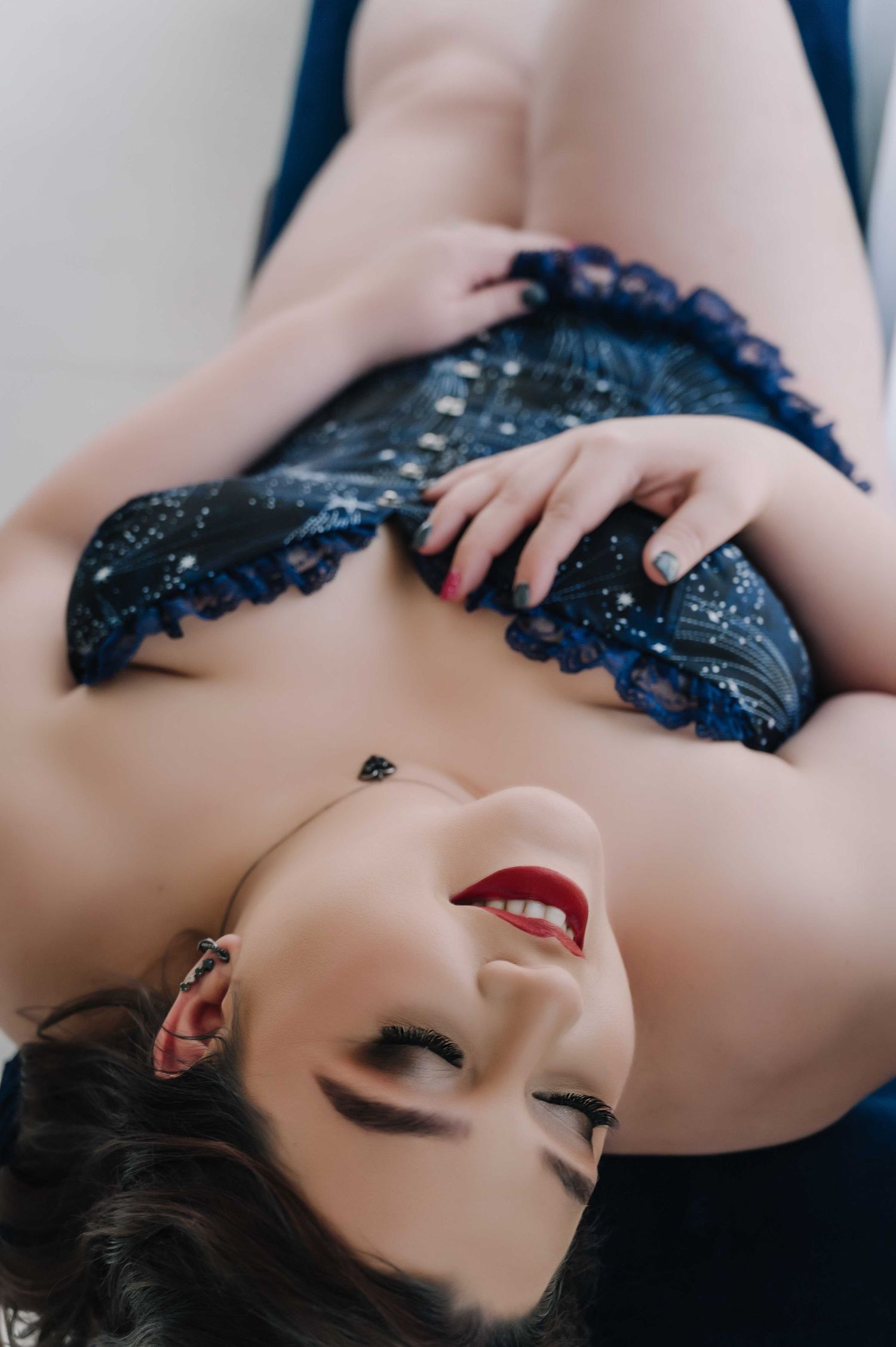 Smiling woman in navy blue lace lingerie, reclining and showing joy during her boudoir session